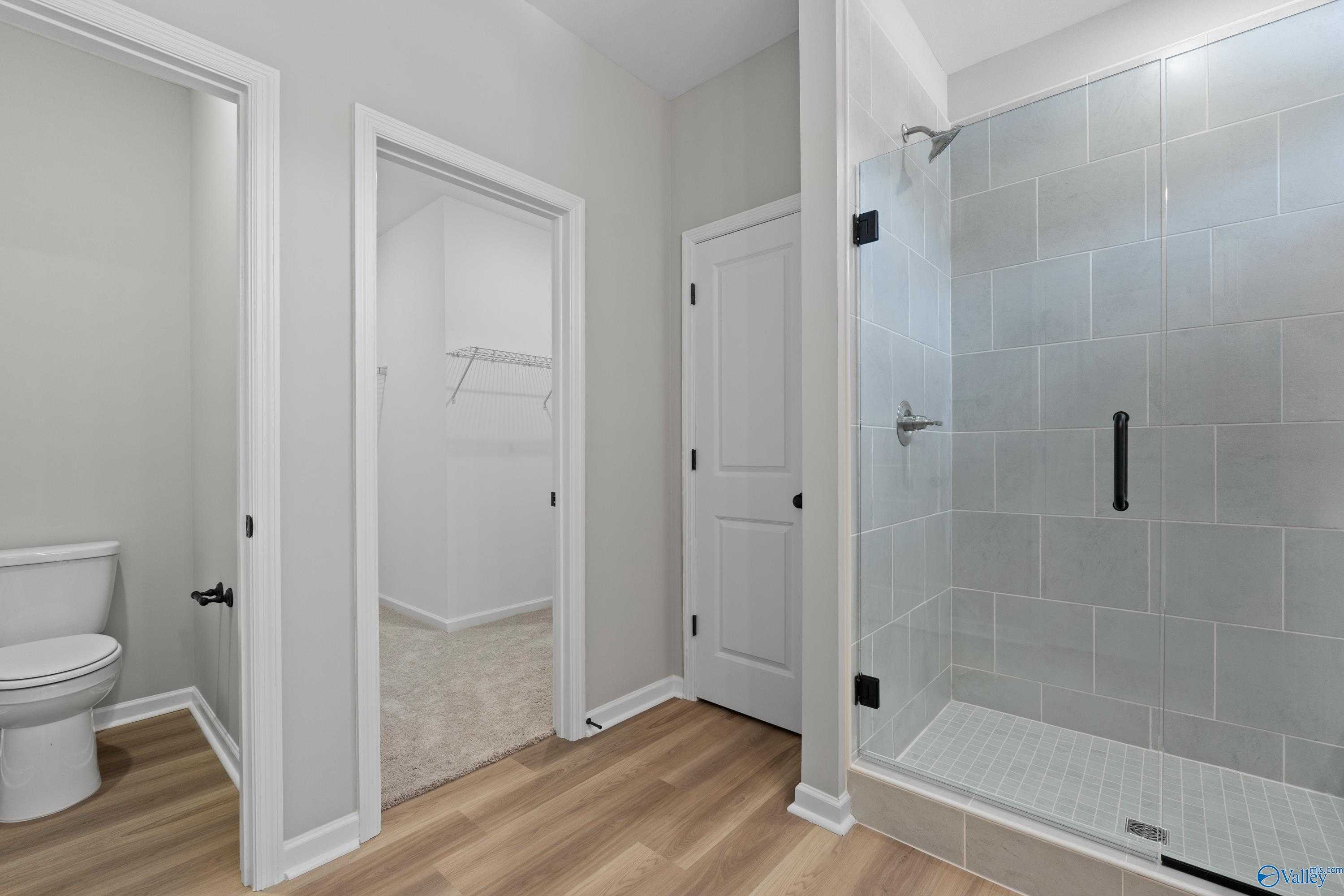Modern master bathroom with tiled glass shower, white toilet, and adjacent walk-in closet in Davidson Homes The Phoenix, Fayetteville, TN