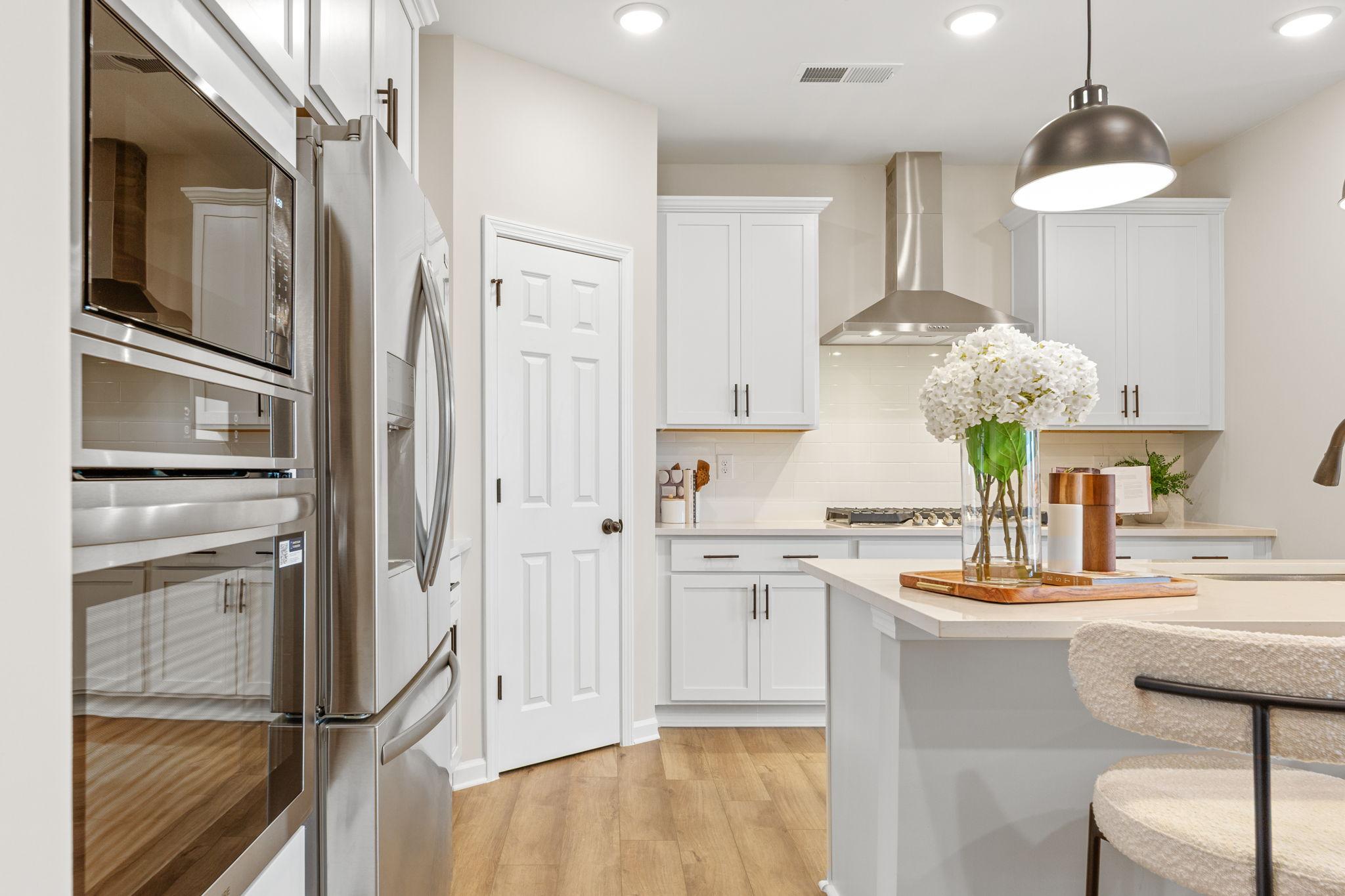 Modern white kitchen featuring stainless steel double oven, island with bar stools and floral centerpiece in Davidson Homes The Durham B, Cumming, GA