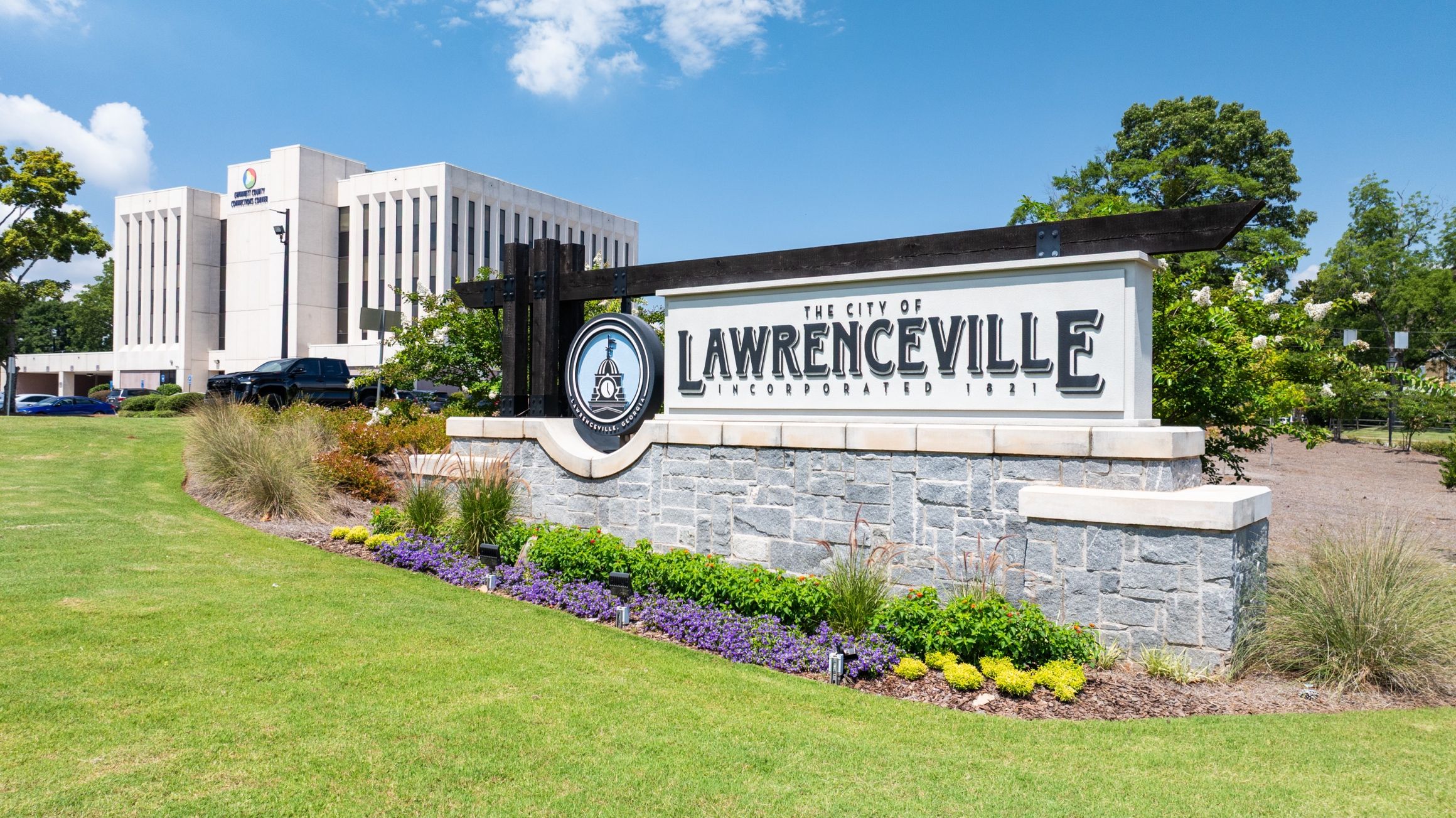 City of Lawrenceville welcome sign in Georgia with stone base, landscaped flowers, and Gwinnett County courthouse behind