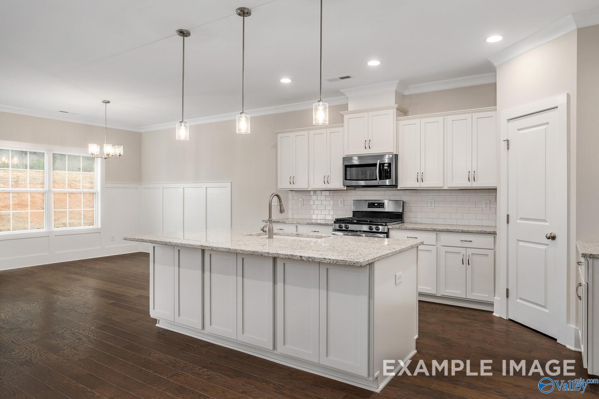 Modern white kitchen featuring granite island, stainless appliances, and pendant lights in Davidson Homes The Rockford, Harvest, Alabama