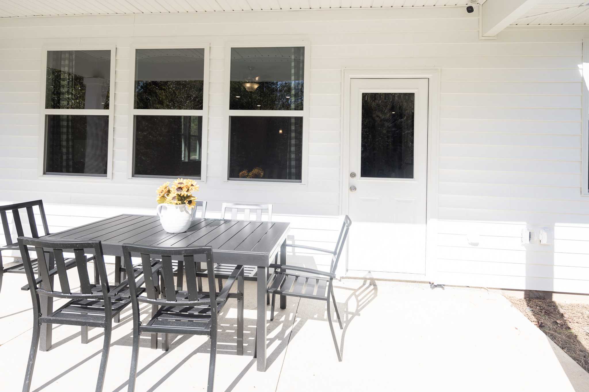 Spacious covered patio at Silver Oak in Cusseta Alabama with black metal dining table chairs and sunflower vase by Evermore Homes
