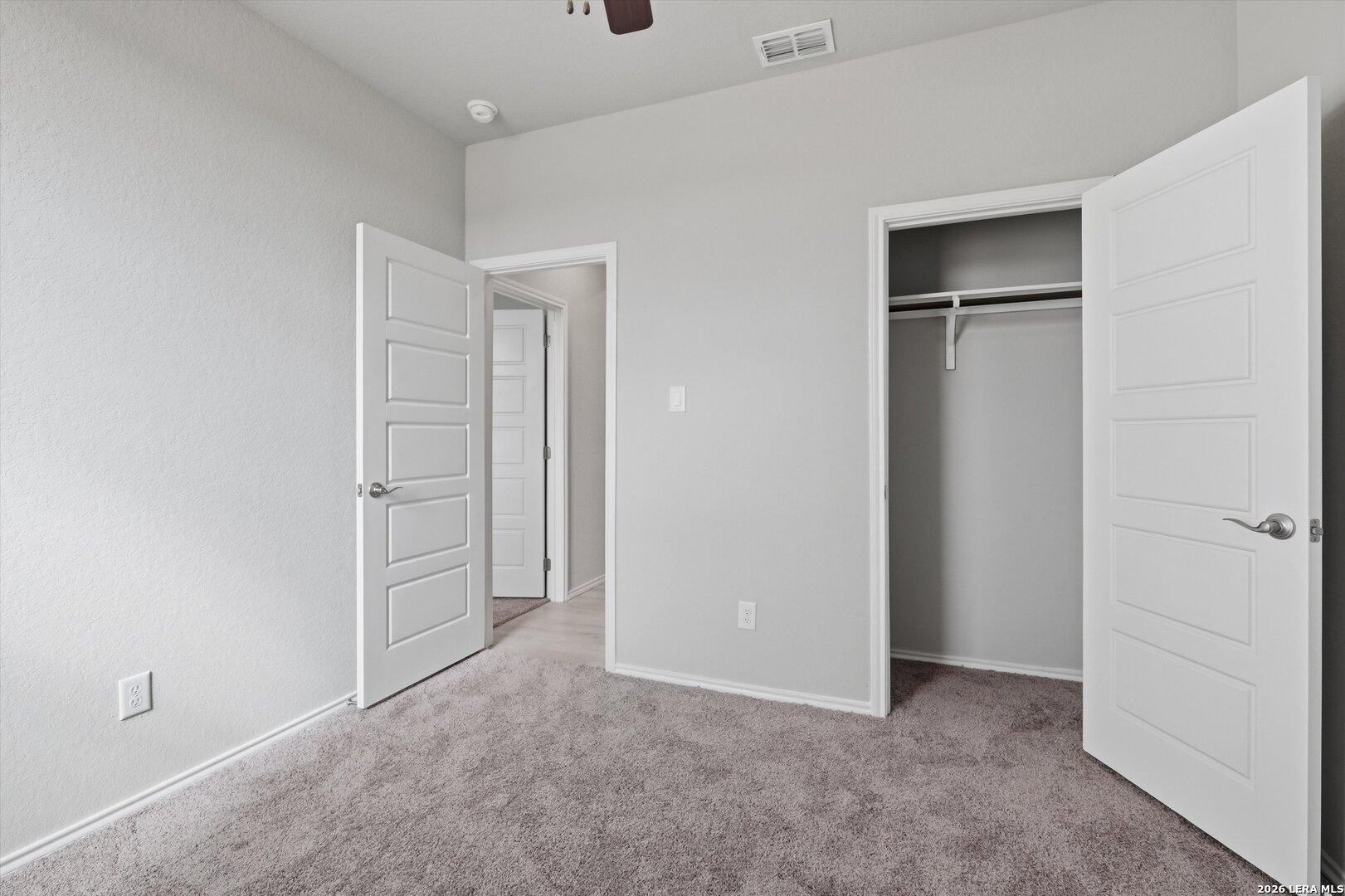 Secondary bedroom with open closet doors, ceiling fan, and gray walls in Davidson Homes The Frio B, Agave, San Antonio