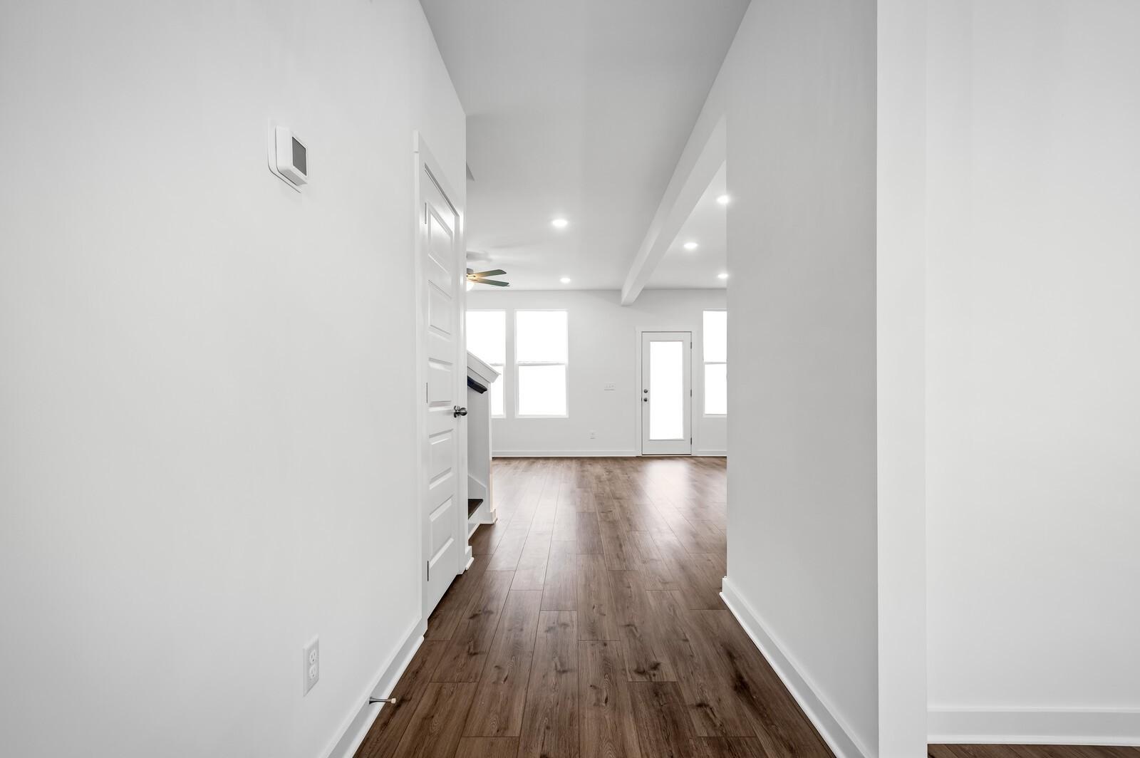 Bright open hallway with wood-style flooring leading to living area in The Willow floor plan at Calista Farms, White House.