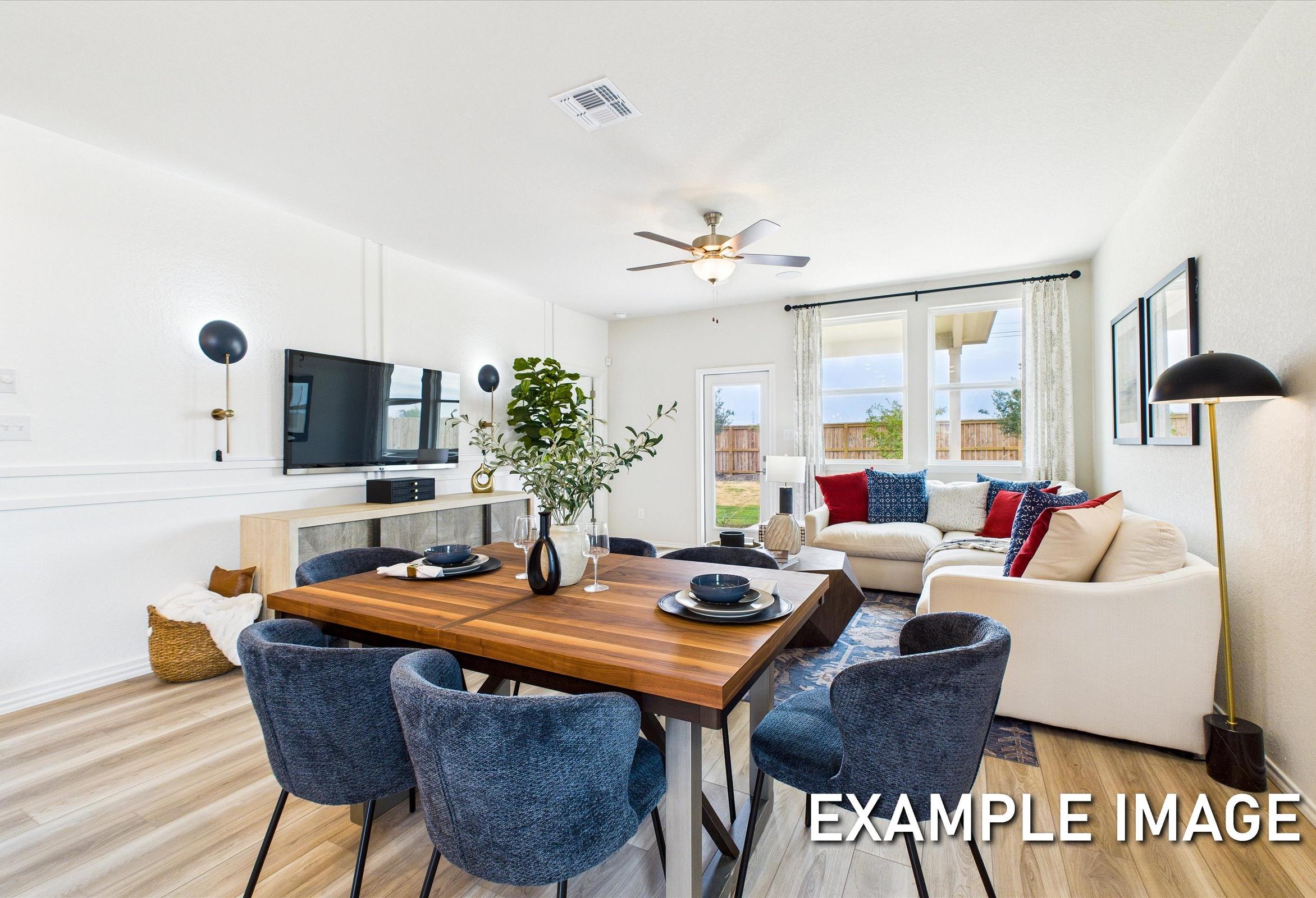 Spacious open-concept living and dining in The Brazos A by Davidson Homes, with wooden table, blue chairs, white sectional, TV, and large windows