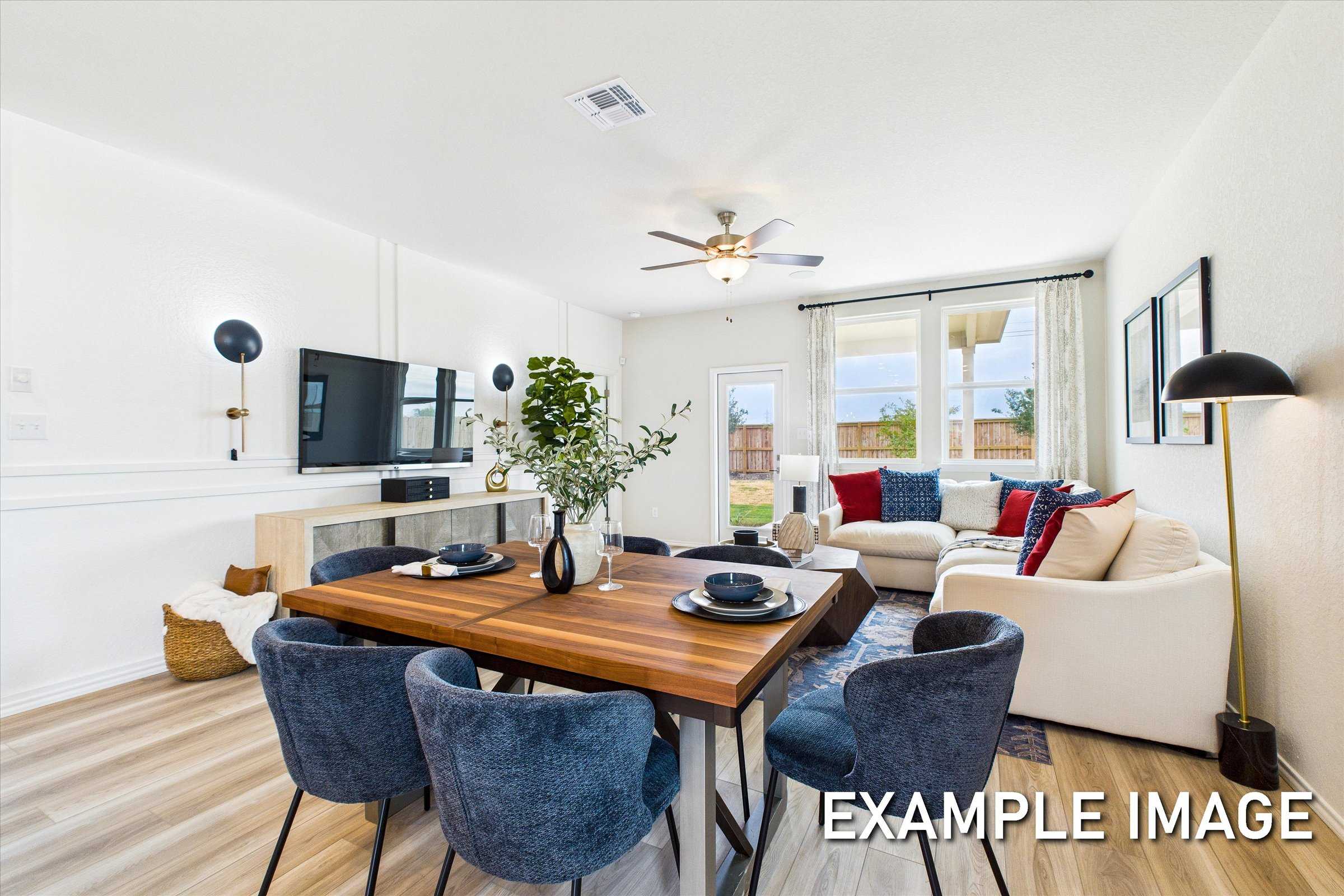 Spacious open-concept living and dining in The Brazos A by Davidson Homes, with wooden table, blue chairs, white sectional, TV, and large windows