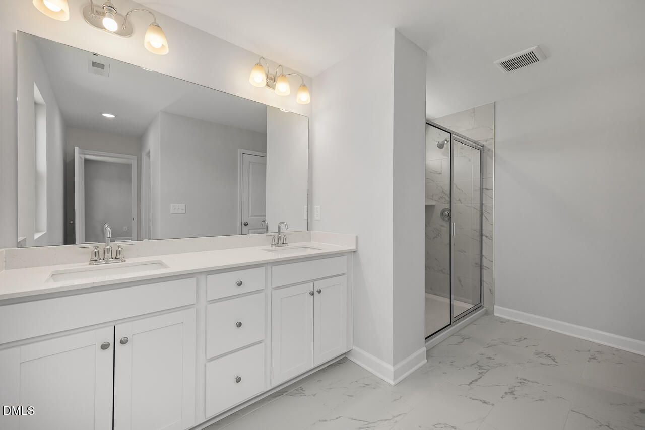 Modern primary bathroom with double vanity and glass-enclosed shower in The Adalynn A at Gregory Village, Lillington, NC.