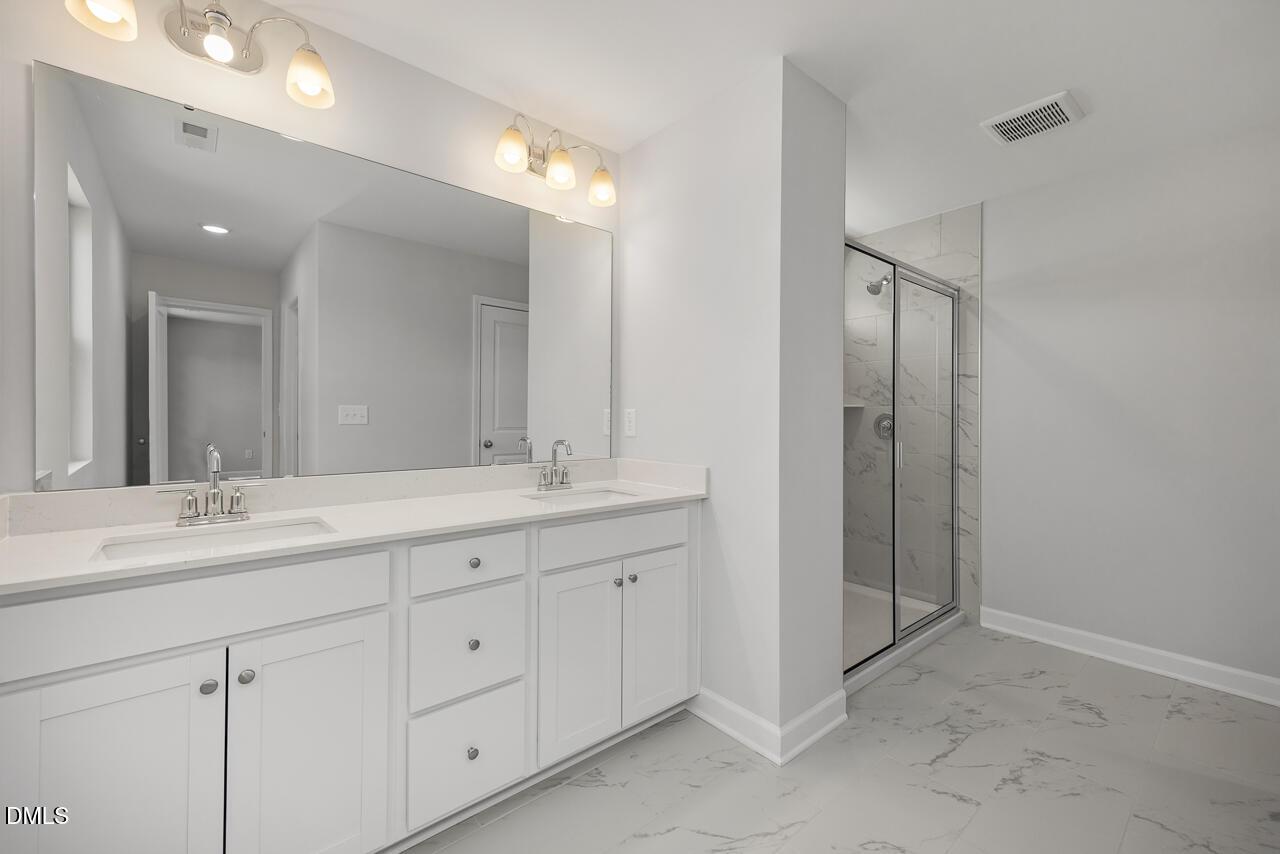 Modern primary bathroom with double vanity and glass-enclosed shower in The Adalynn A at Gregory Village, Lillington, NC.