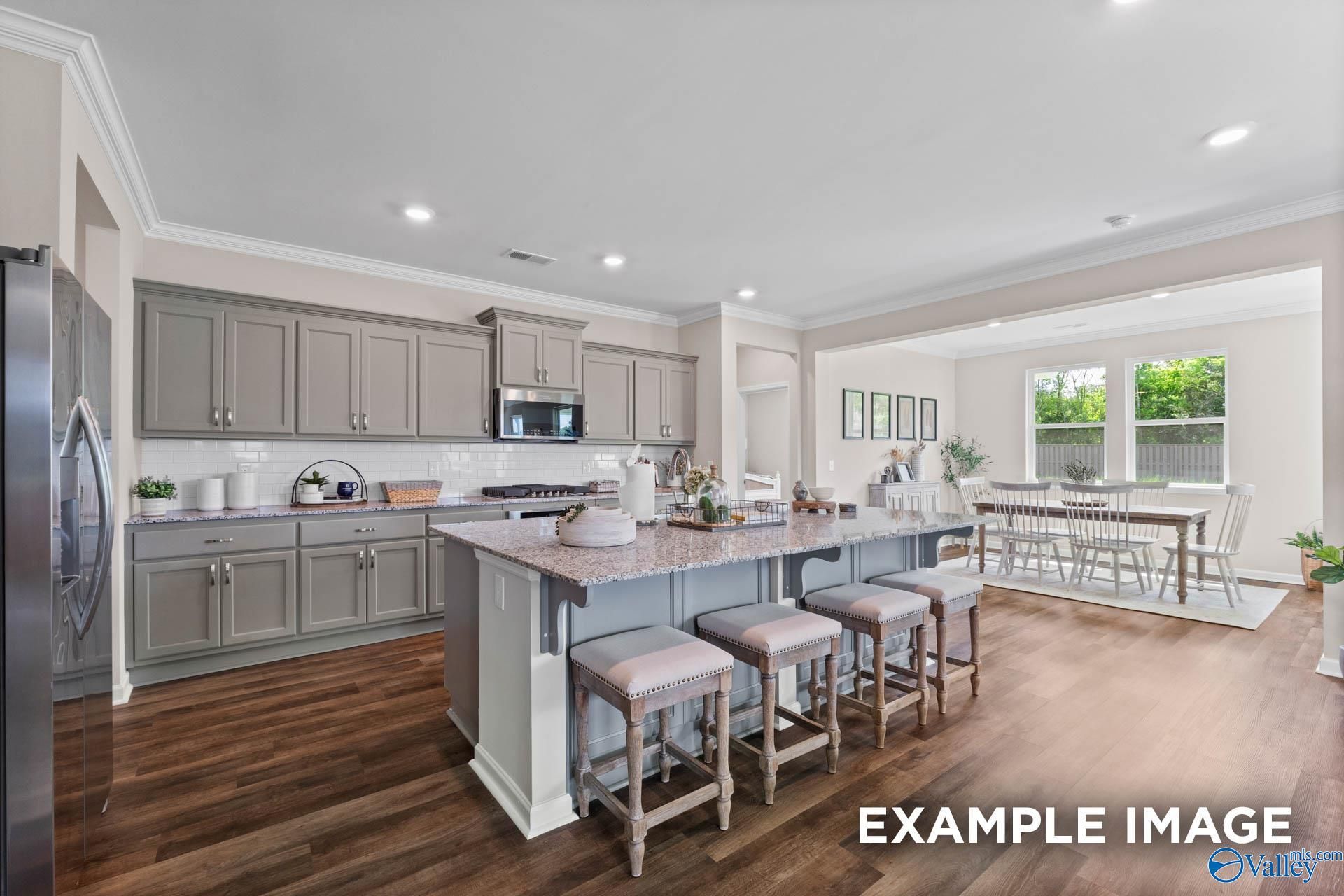 Modern gray shaker kitchen with large island, bar stools, and open dining area in The Arcadia M by Evermore Homes, Owens Cross Roads, AL