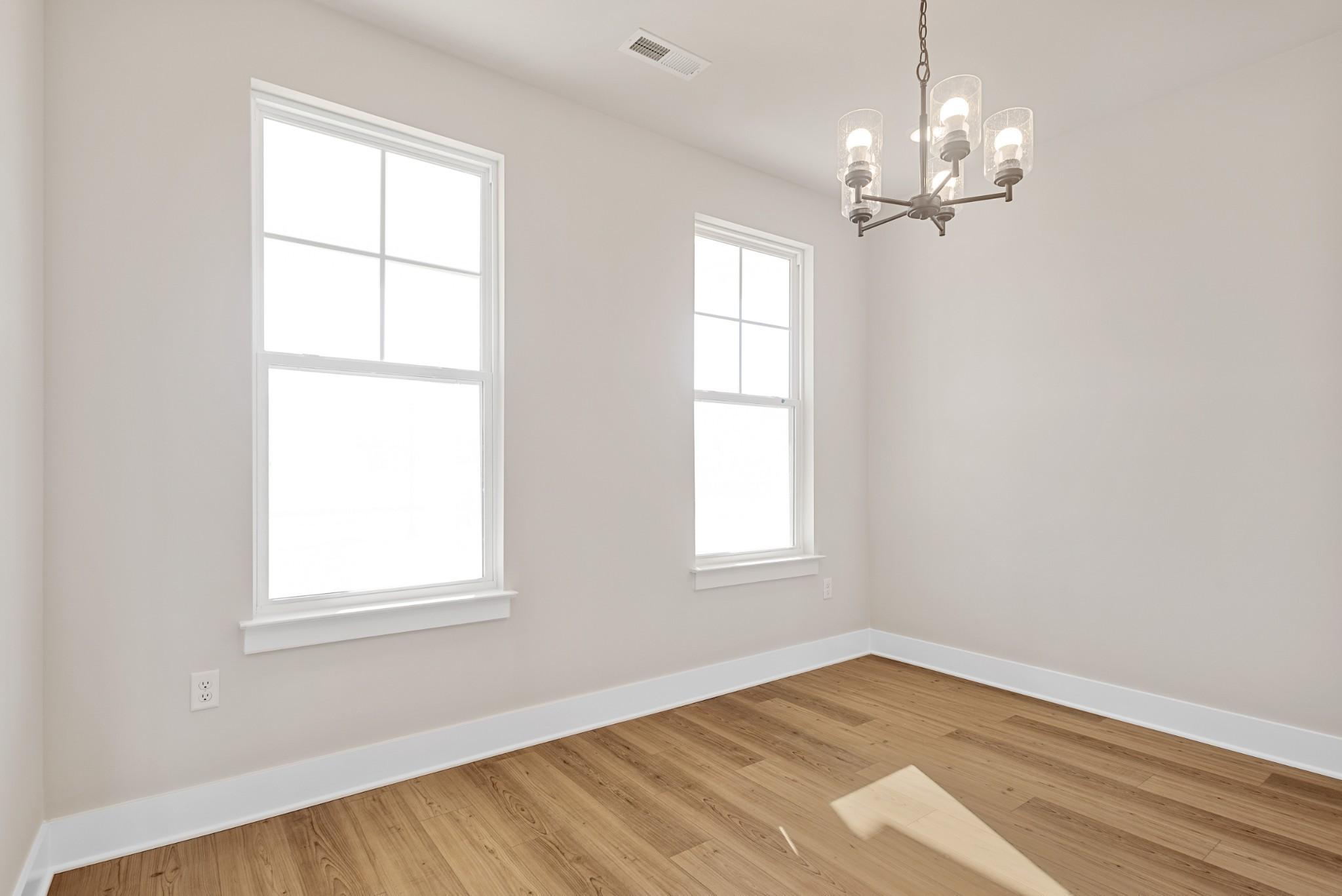 Bright, modern bedroom with hardwood floors, large windows, and elegant chandelier in Willow B plan, Calista Farms, TN.