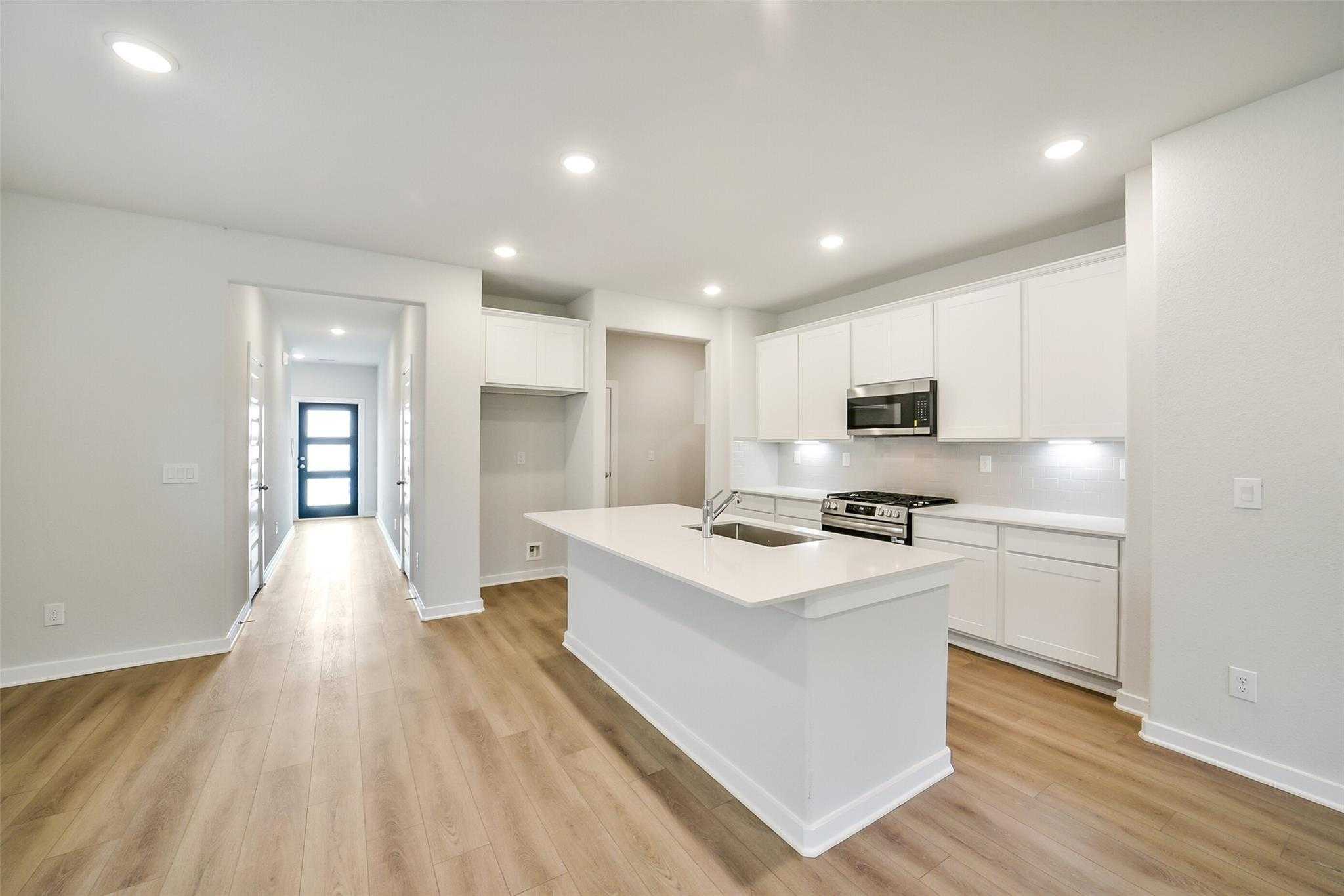 Modern white kitchen with island, stainless appliances, and open hallway in Davidson Homes Blanco E, Magnolia Texas