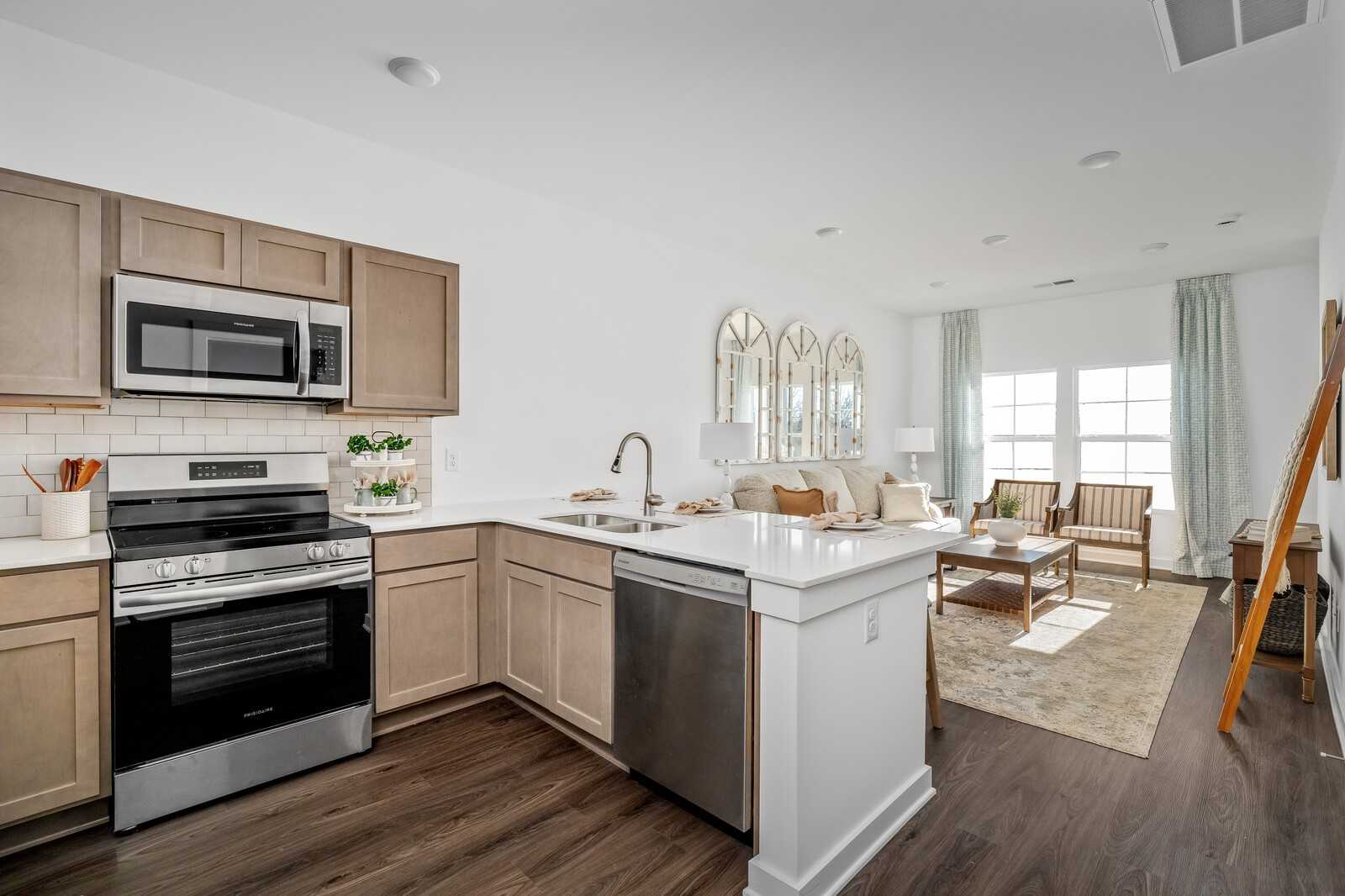 Modern open-concept kitchen-living area with beige shaker cabinets, stainless appliances, white quartz island, and cozy beige sofa in Davidson Homes The Cumberland A, Gallatin TN