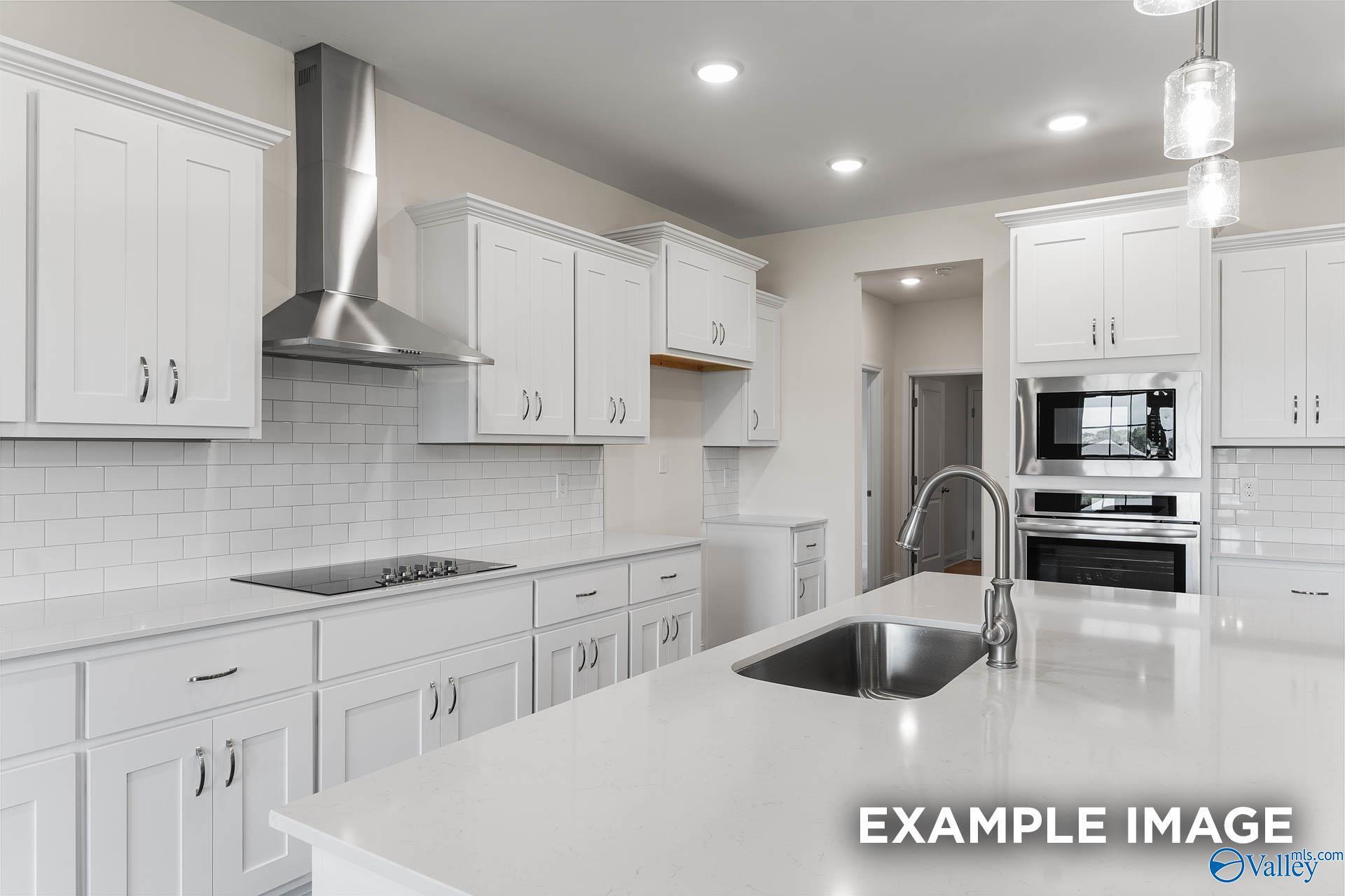 Modern white kitchen with stainless steel appliances, subway tile backsplash, and large island in The Emory floor plan, Toney, Alabama