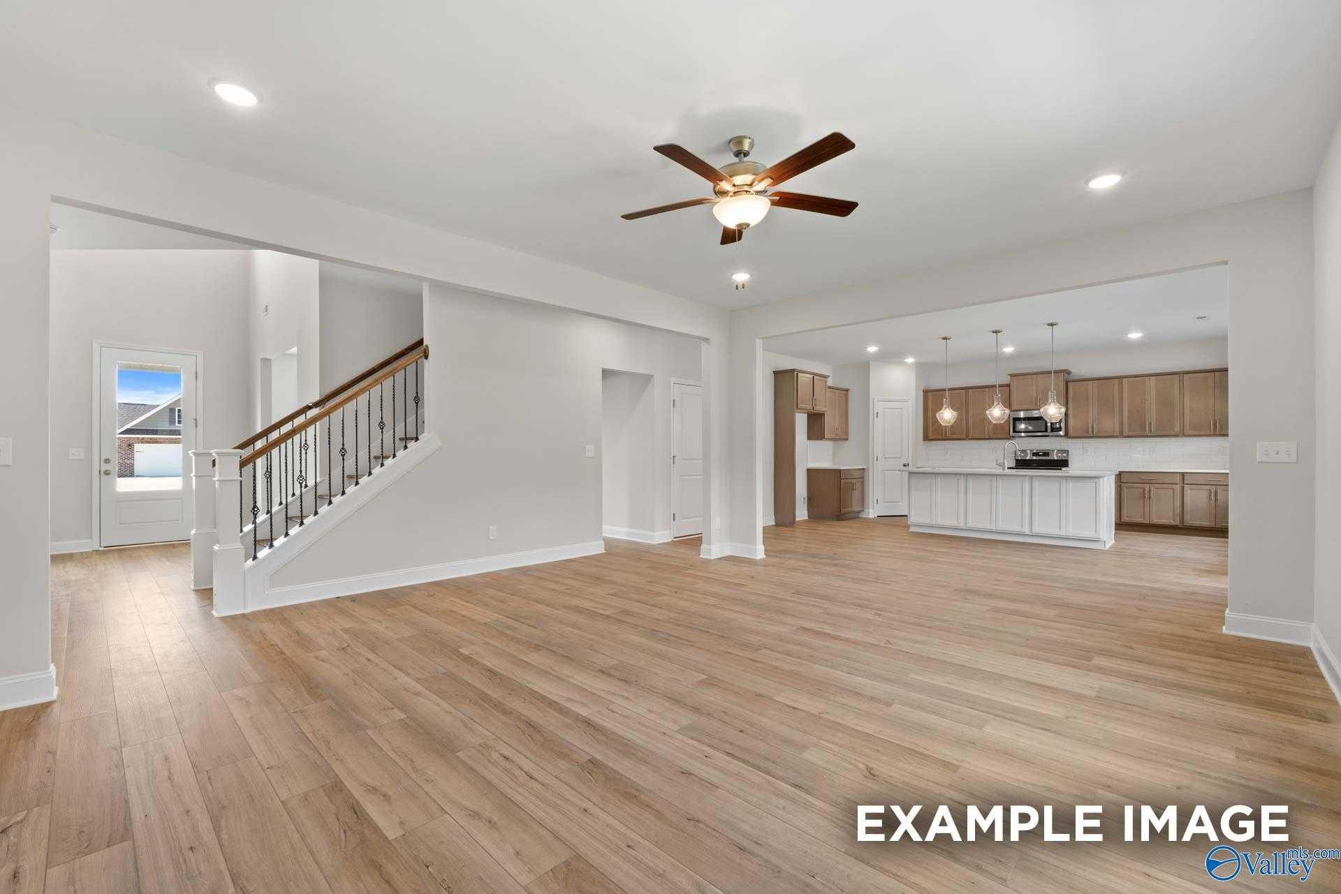 Open two-story foyer with hardwood floors, wooden staircase, ceiling fan, and adjacent modern kitchen in Davidson Homes The Madison A, Meridianville