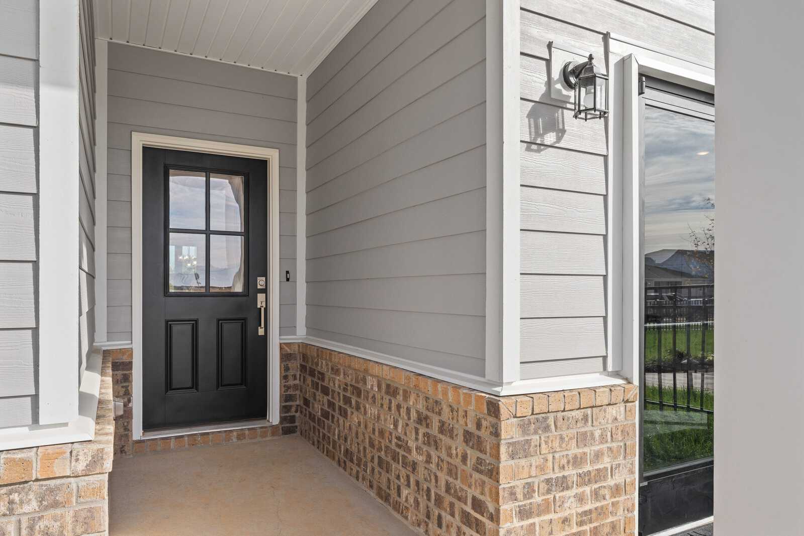 Covered front porch entrance at Sage Farms in White House TN with gray siding, brick accents, and black glass door