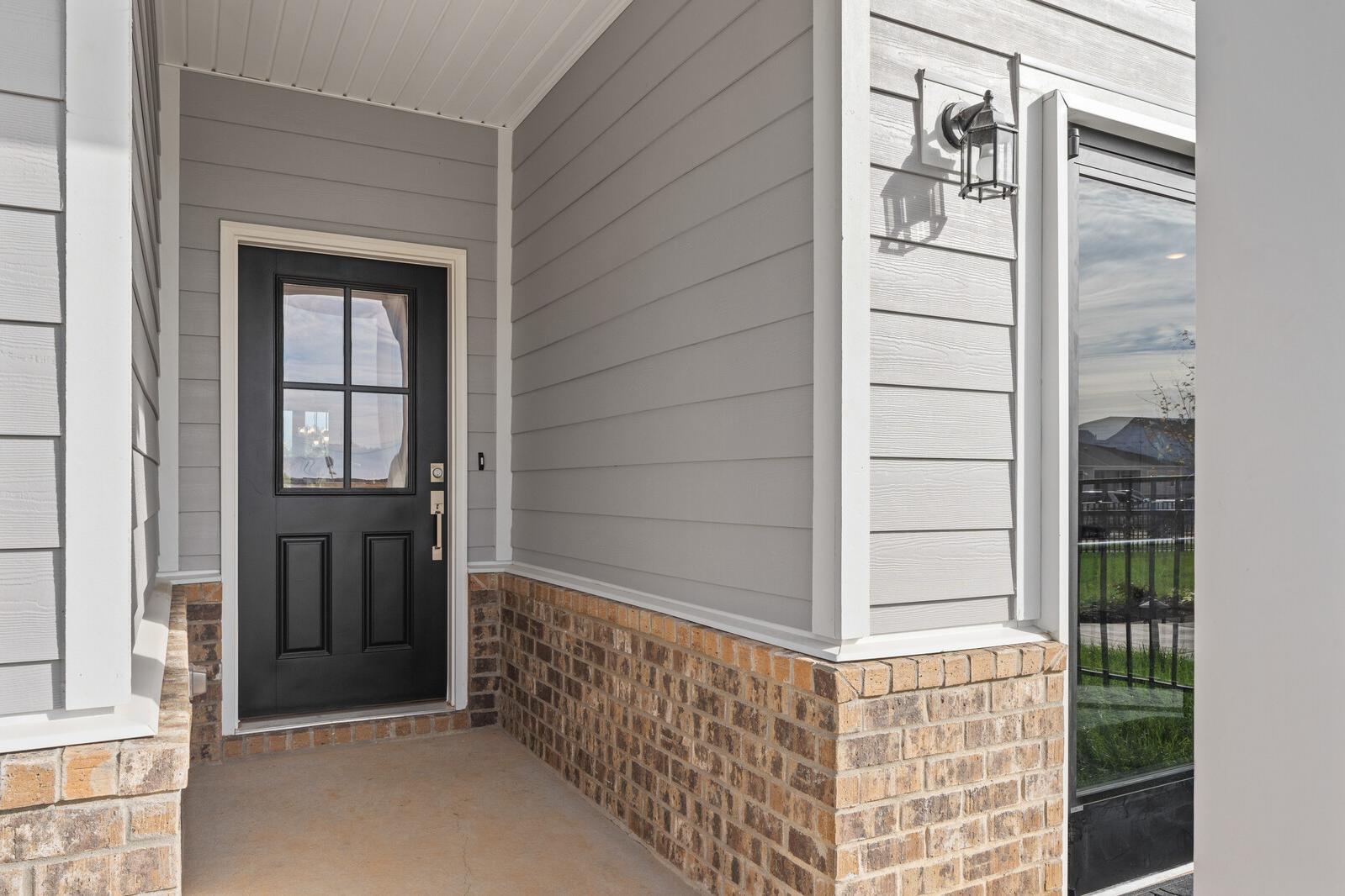 Covered front porch entrance at Sage Farms in White House TN with gray siding, brick accents, and black glass door