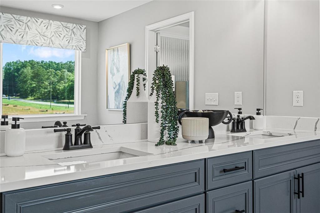 Elegant master bathroom double vanity with quartz counters, navy cabinets, greenery accents, and lush outdoor view in Davidson Homes Hickory B, Hoschton, GA
