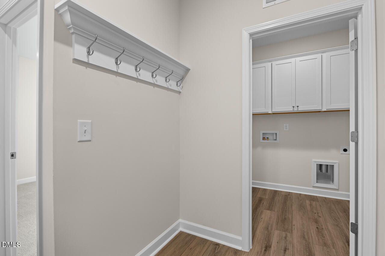 Coat rack with hooks beside laundry room with white cabinets and wood-look flooring in Davidson Homes Birch II C, Wake Forest