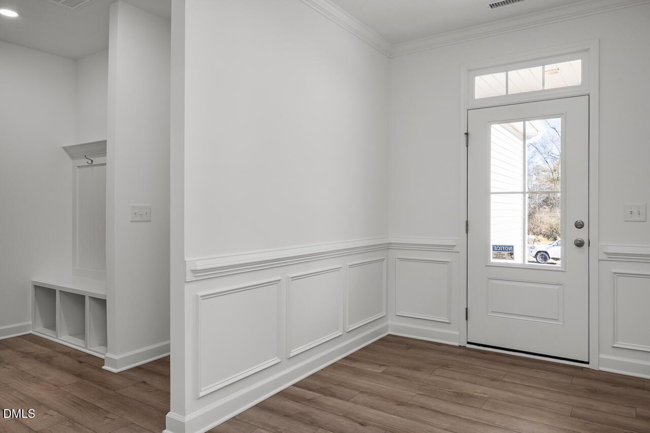 Bright entryway with white wainscoting, coat hooks, built-in bench, and glass door in Davidson Homes The Cypress B II, Angier, NC