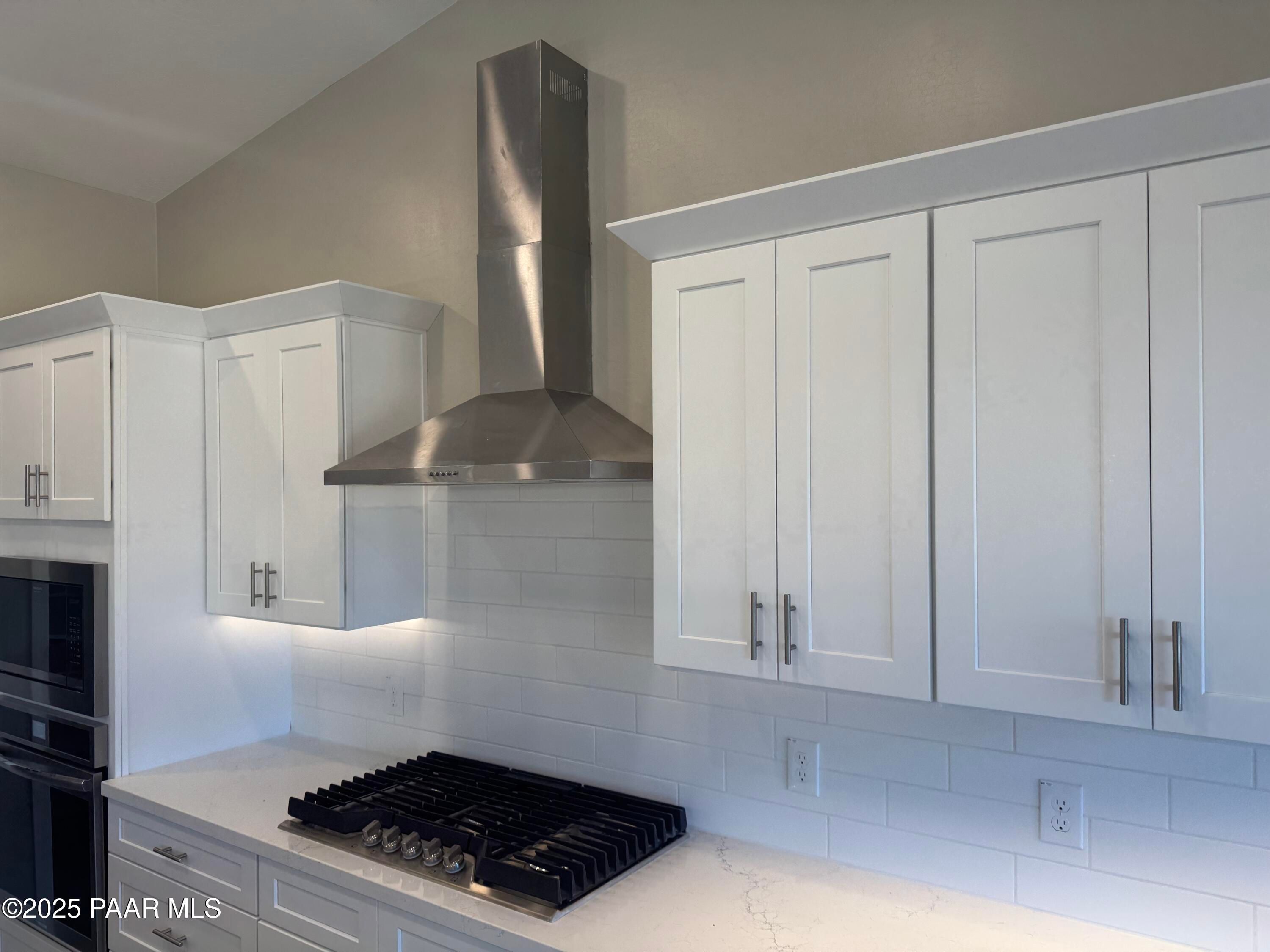 Modern white kitchen featuring stainless steel range hood, quartz counters, gas cooktop in Davidson Homes The Monarch E, Prescott AZ