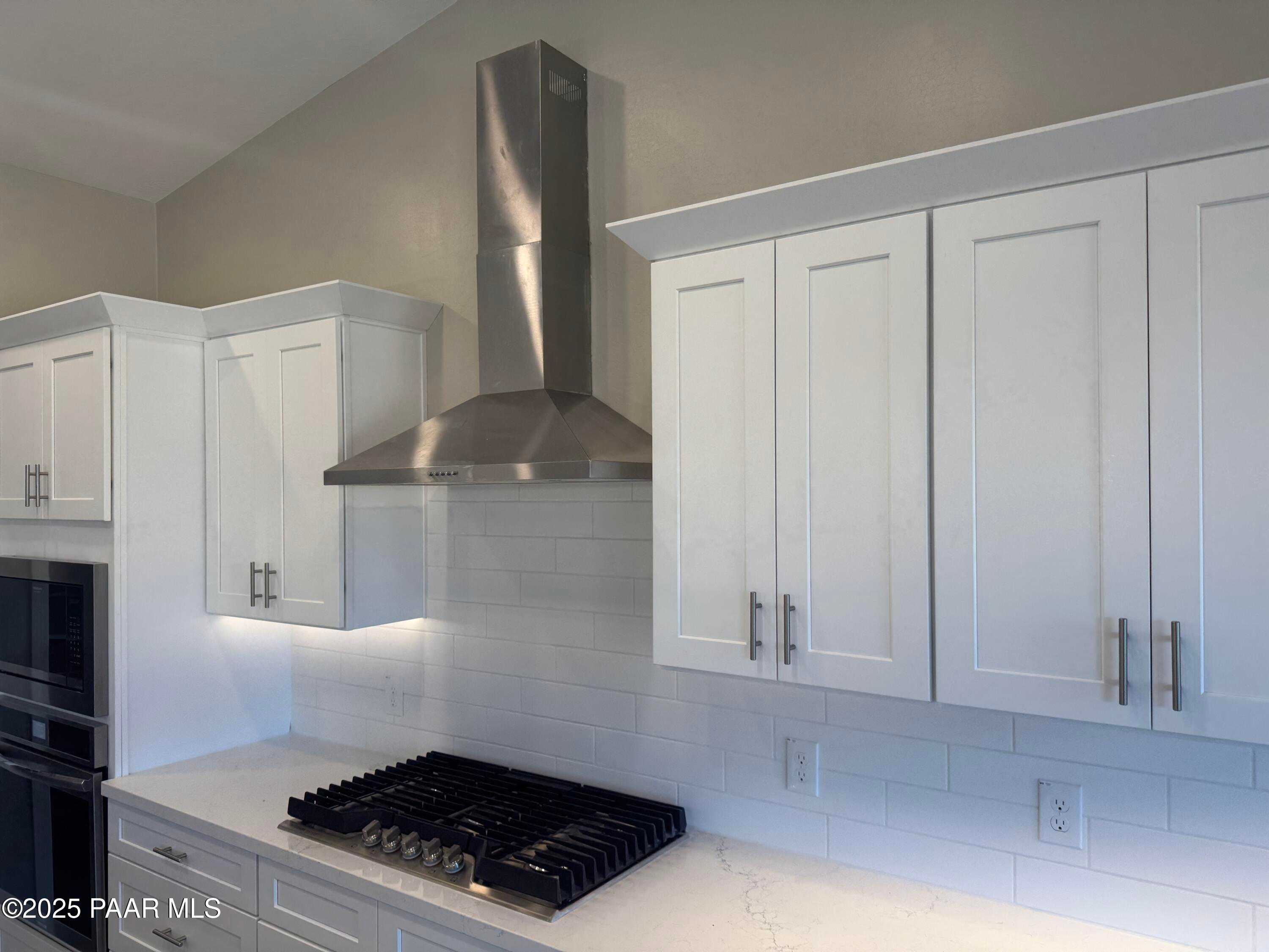 Modern white kitchen featuring stainless steel range hood, quartz counters, gas cooktop in Davidson Homes The Monarch E, Prescott AZ