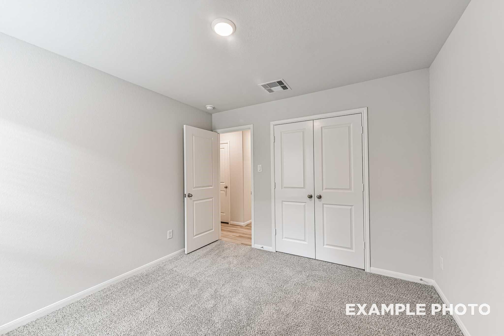Light gray secondary bedroom with carpet flooring, double closet doors, and bathroom entry in Davidson Homes The Riviera A, Rosharon, Texas