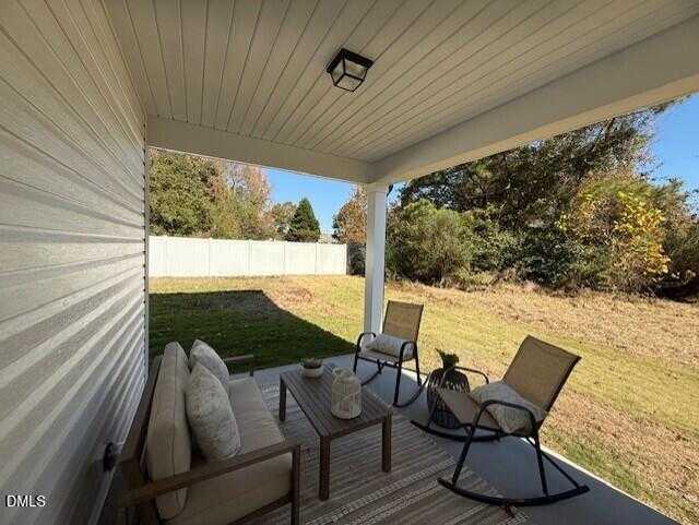 Covered back patio with beige sofa, rattan chairs, and plants overlooking fenced yard in Davidson Homes Preston C, Lillington, NC