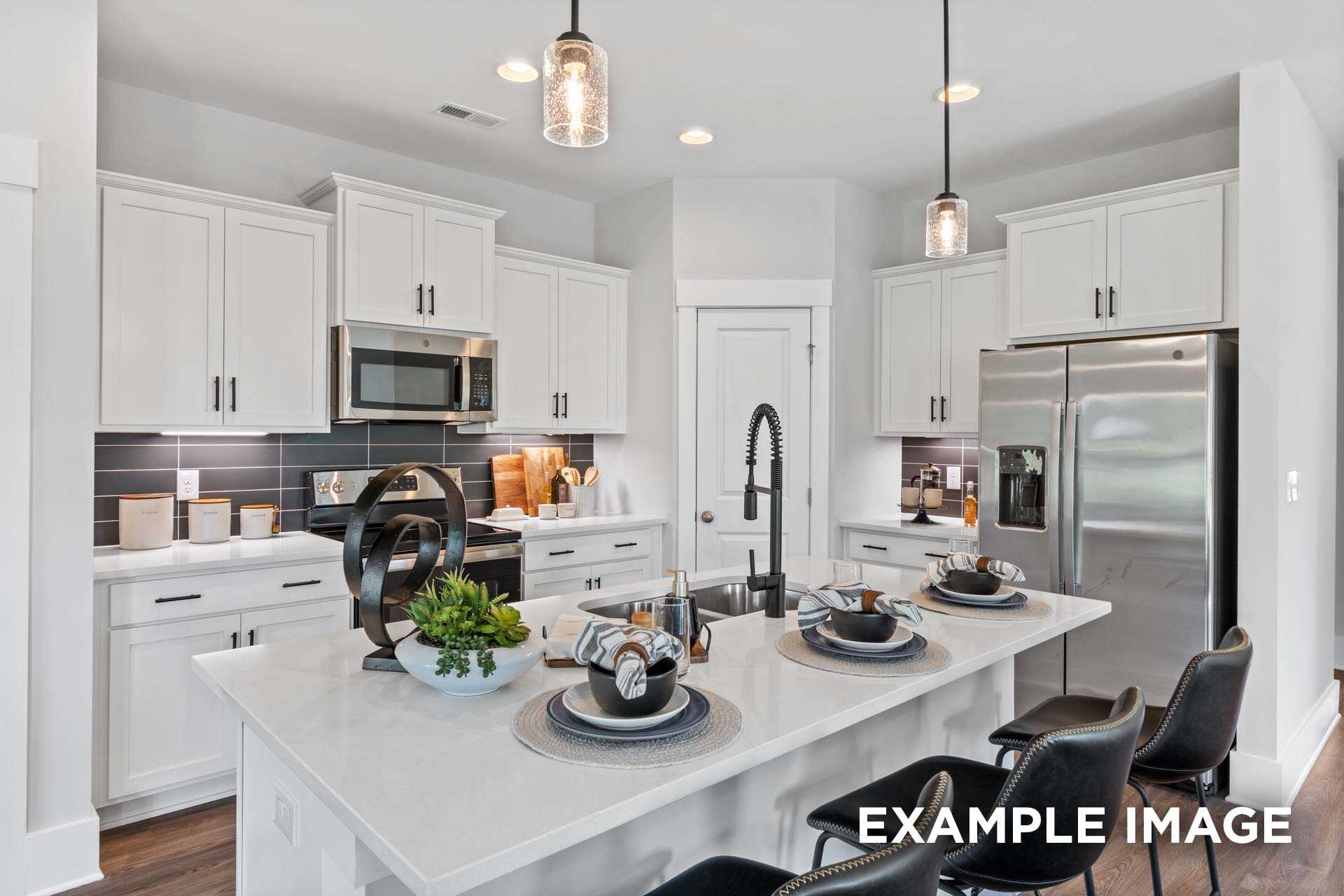 Spacious modern kitchen in The Franklin C with white shaker cabinets, quartz island, stainless appliances, and pendant lights