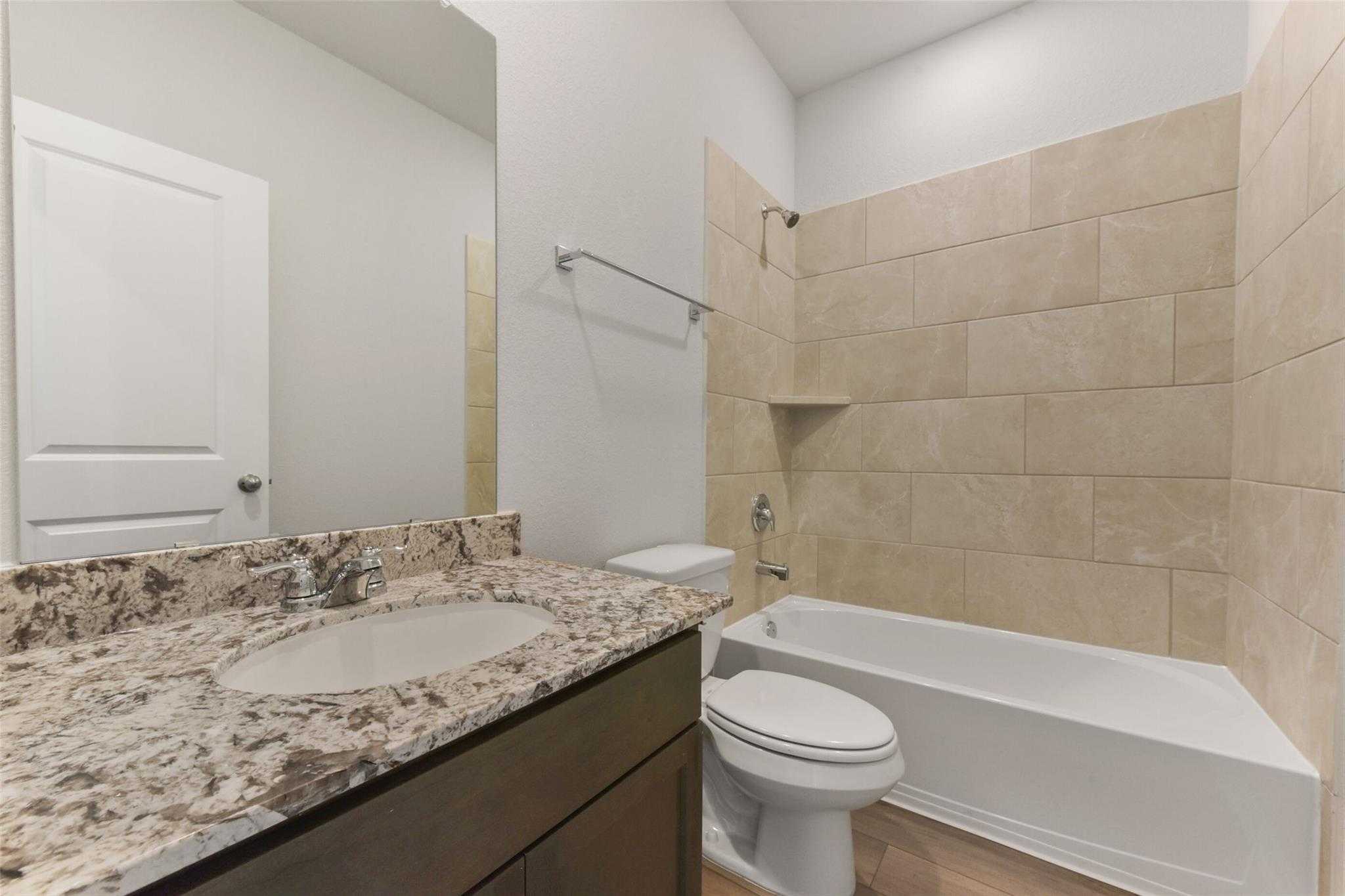 Modern bathroom with granite vanity, beige tiled shower, bathtub, and toilet in Davidson Homes The Laguna B, Magnolia, Texas