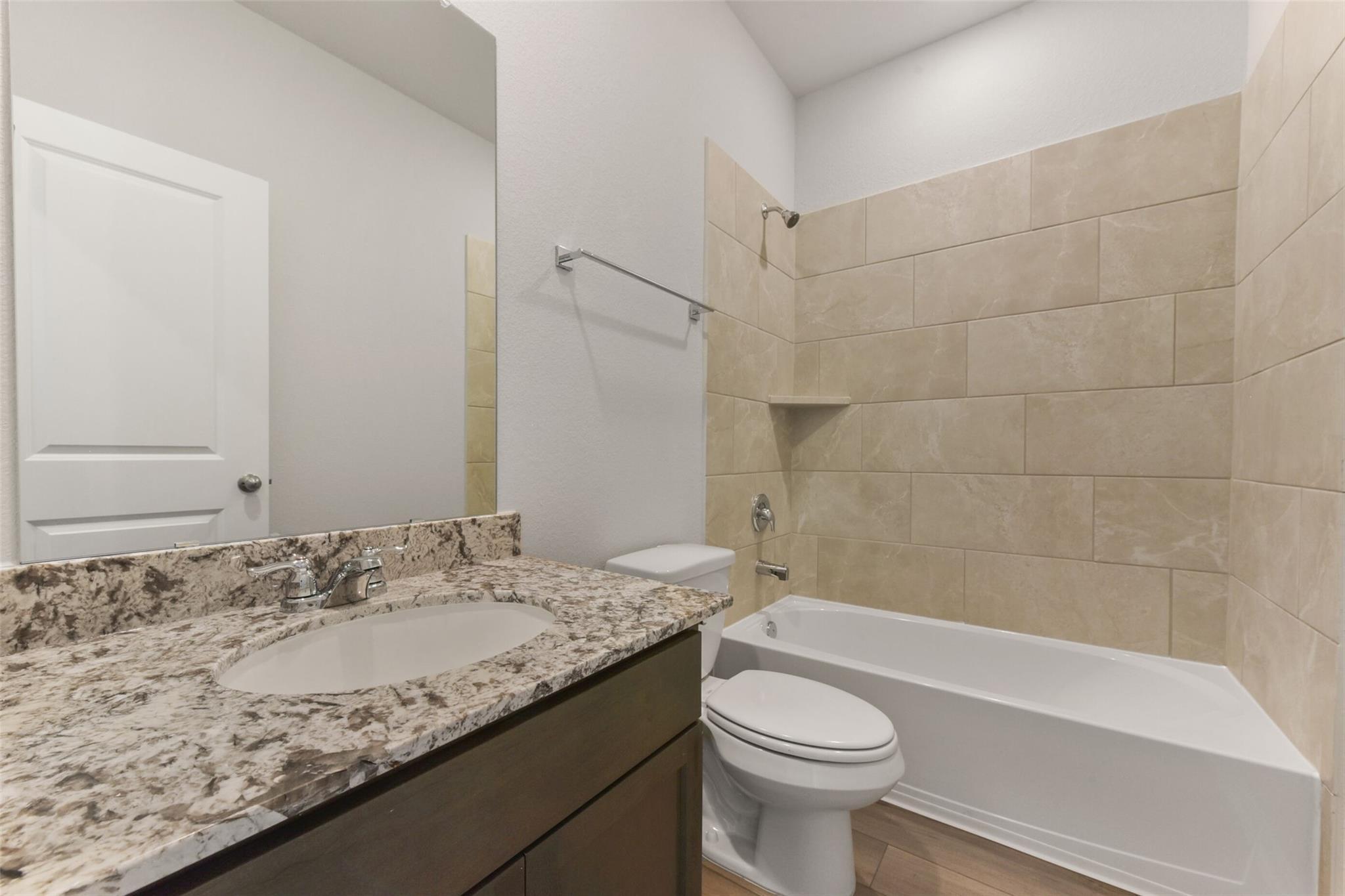 Modern bathroom with granite vanity, beige tiled shower, bathtub, and toilet in Davidson Homes The Laguna B, Magnolia, Texas
