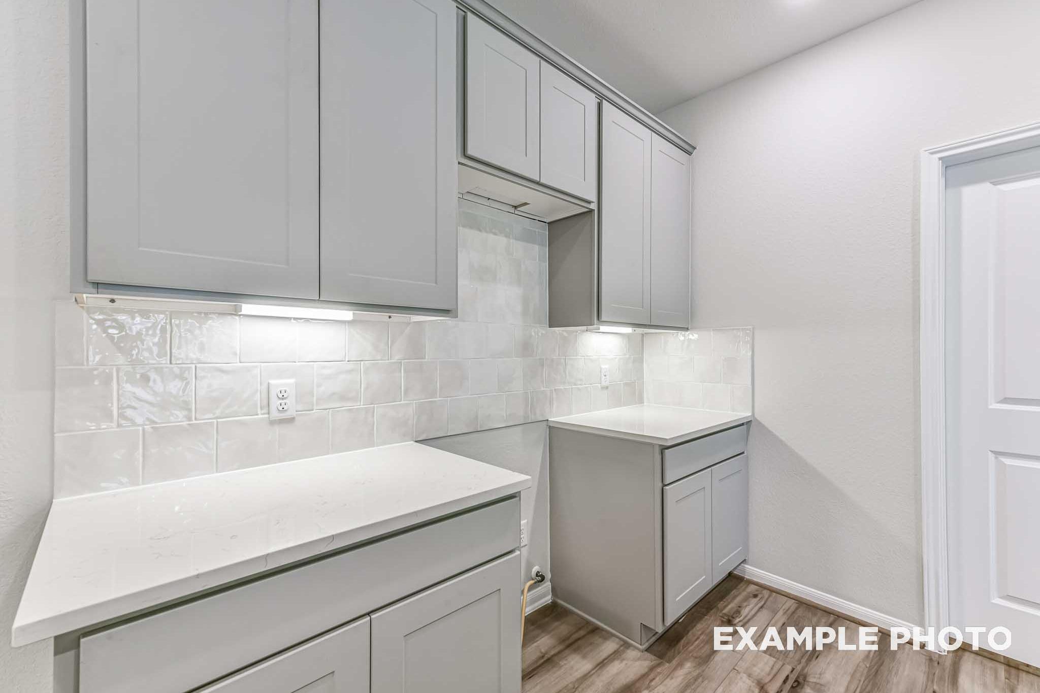 Modern laundry room in The Laguna A home featuring white shaker cabinets, subway tile backsplash, quartz counters, and under-cabinet lighting