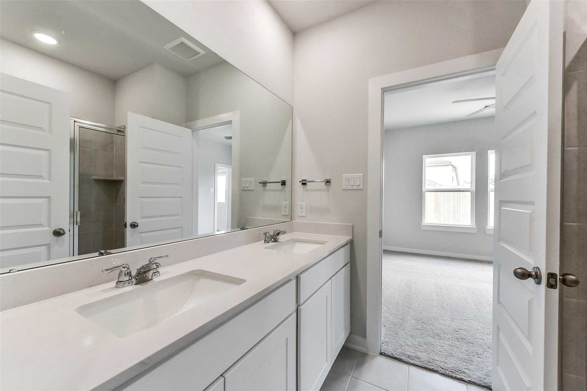 Modern double-sink vanity with white cabinets and large mirror in The Frio F 3-bedroom bathroom, Davidson Homes, Dayton, Texas