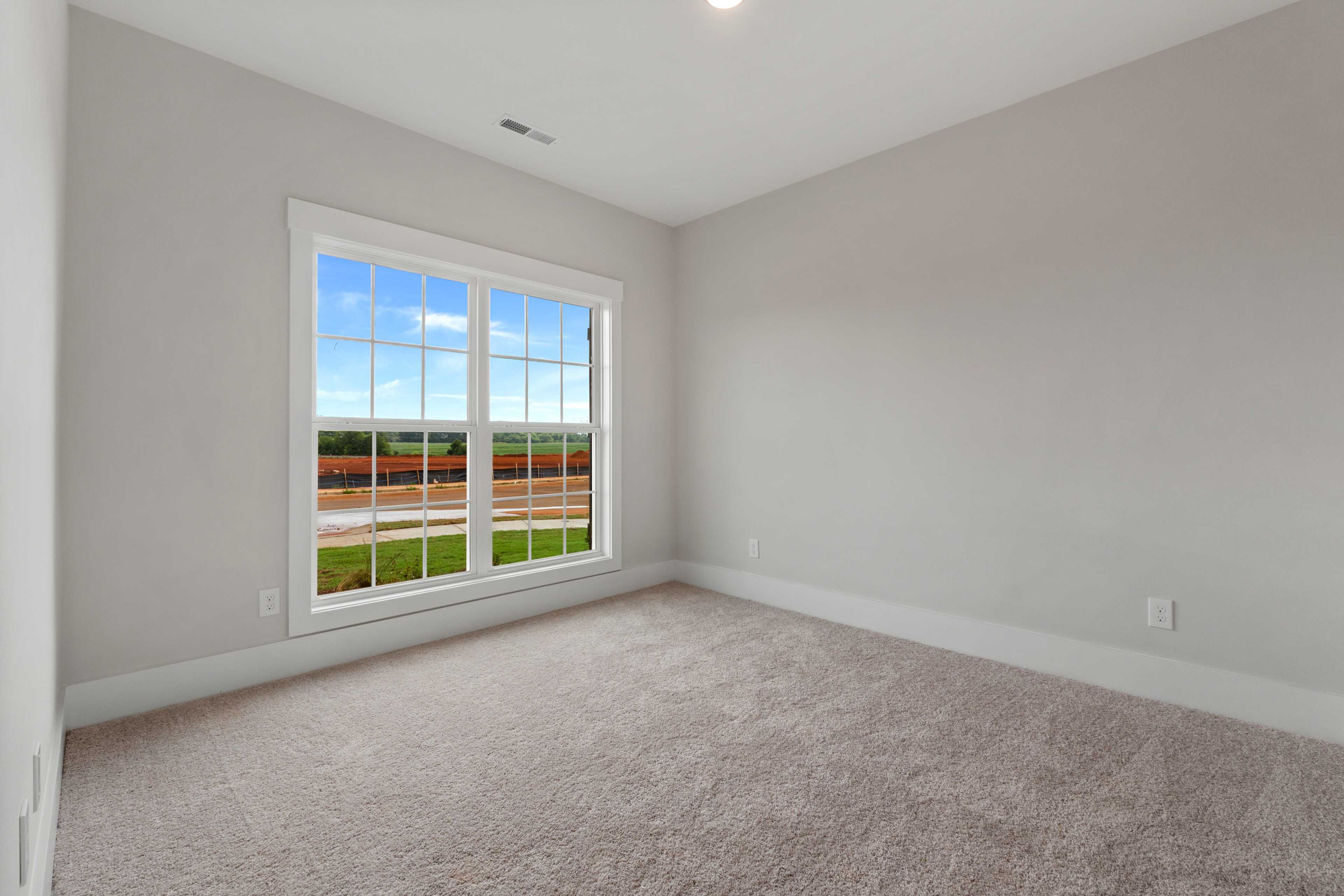 Spacious neutral bedroom with gray walls, beige carpet, and large window overlooking green field at The Villas at Barnett's Crossing in Madison, Alabama