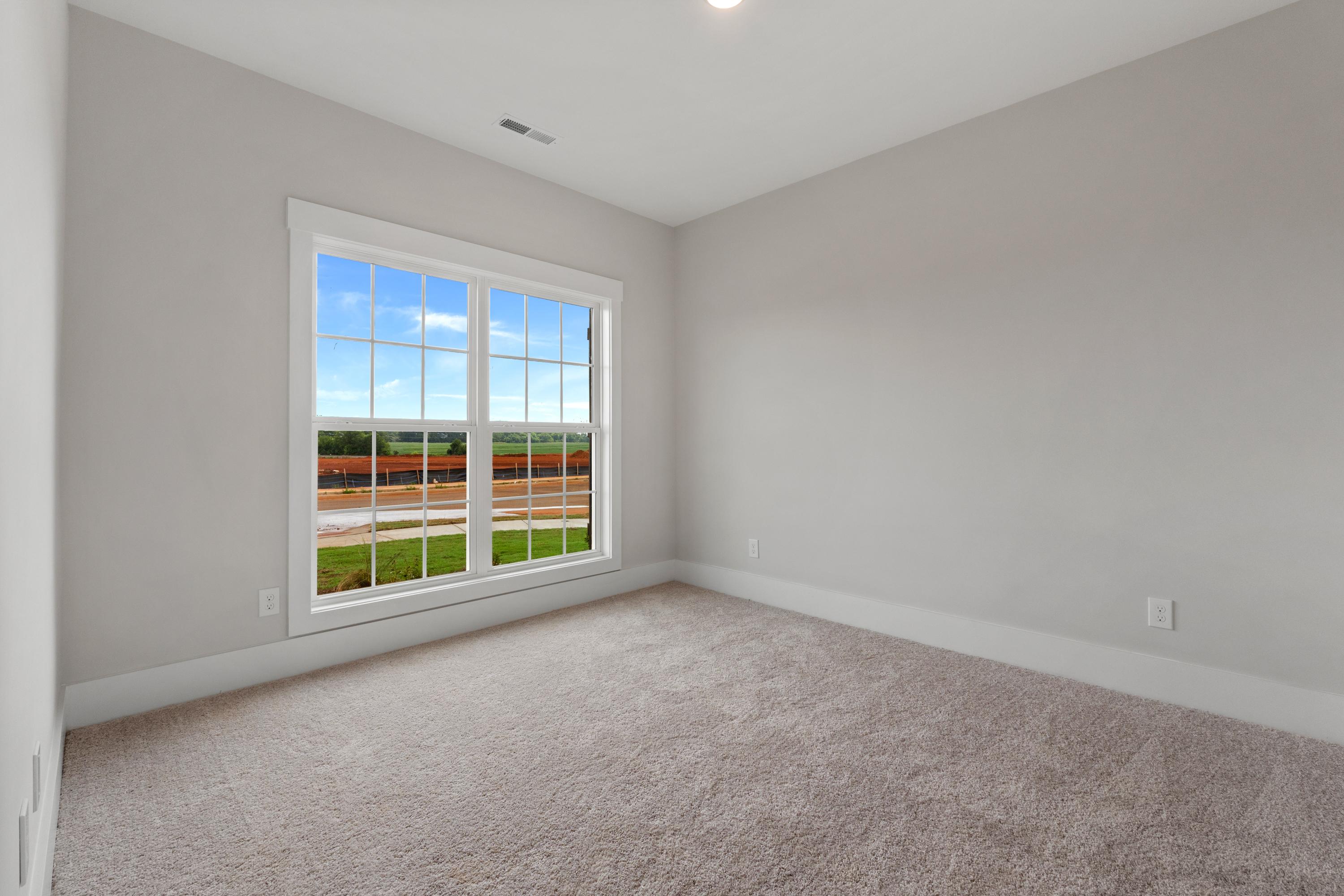 Spacious neutral bedroom with gray walls, beige carpet, and large window overlooking green field at The Villas at Barnett's Crossing in Madison, Alabama