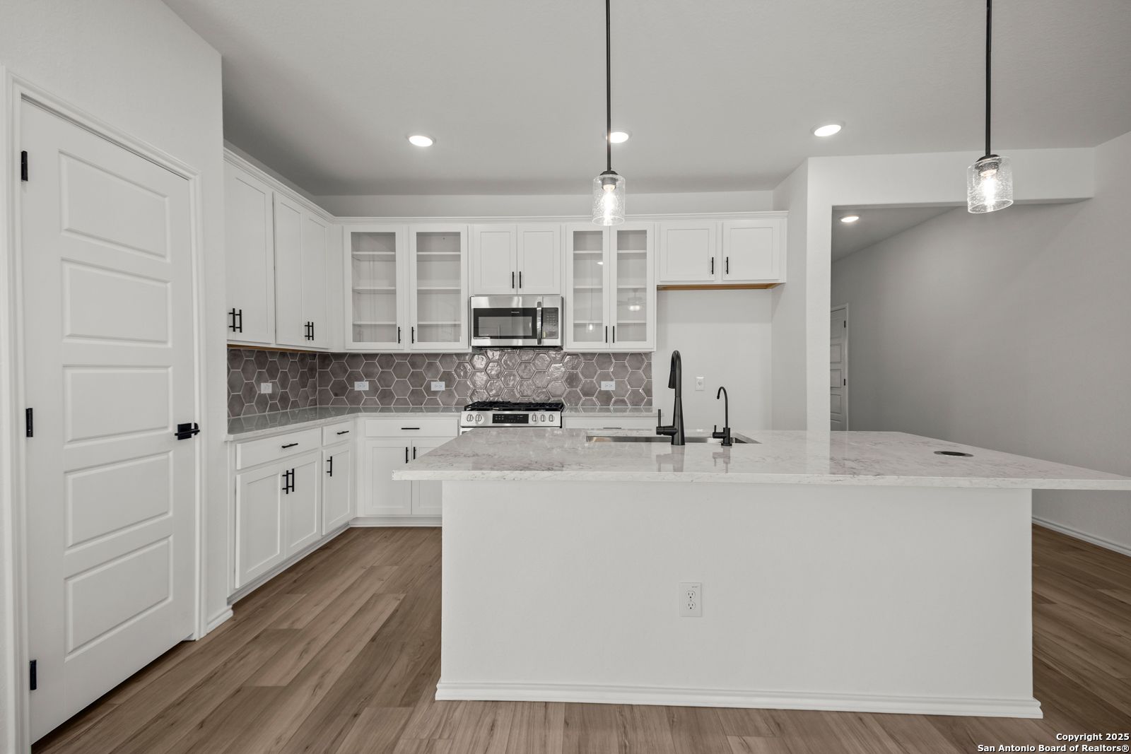 Bright modern kitchen with white shaker cabinets, granite island sink, subway tile backsplash in The Daphne K, San Antonio