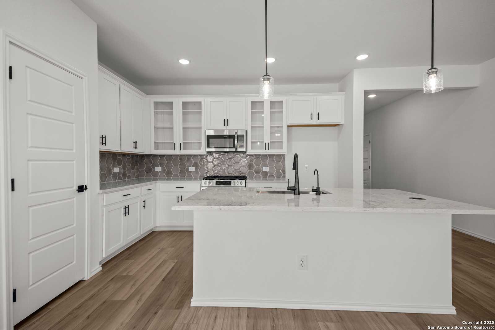 Bright modern kitchen with white shaker cabinets, granite island sink, subway tile backsplash in The Daphne K, San Antonio