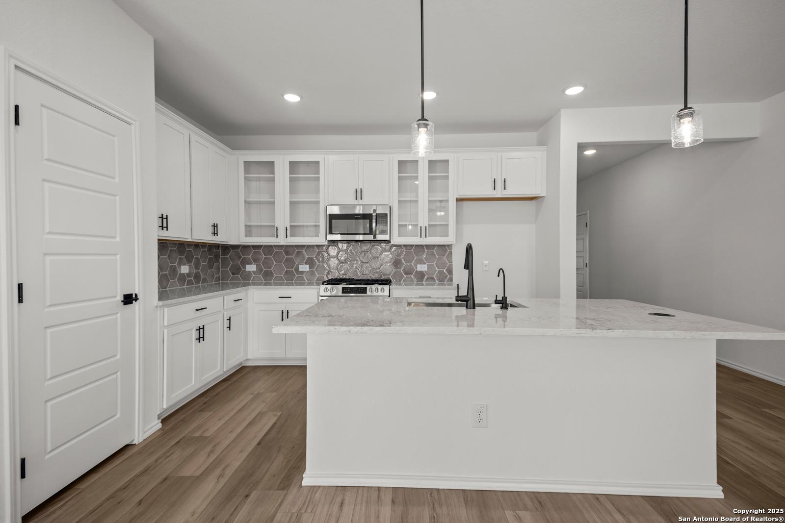 Bright modern kitchen with white shaker cabinets, granite island sink, subway tile backsplash in The Daphne K, San Antonio