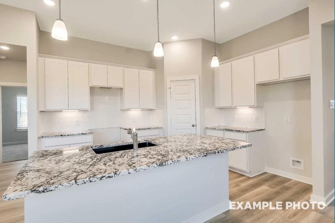 Modern white kitchen with granite island sink, pendant lights, and subway backsplash in Davidson Homes The Riviera C, Dayton, Texas