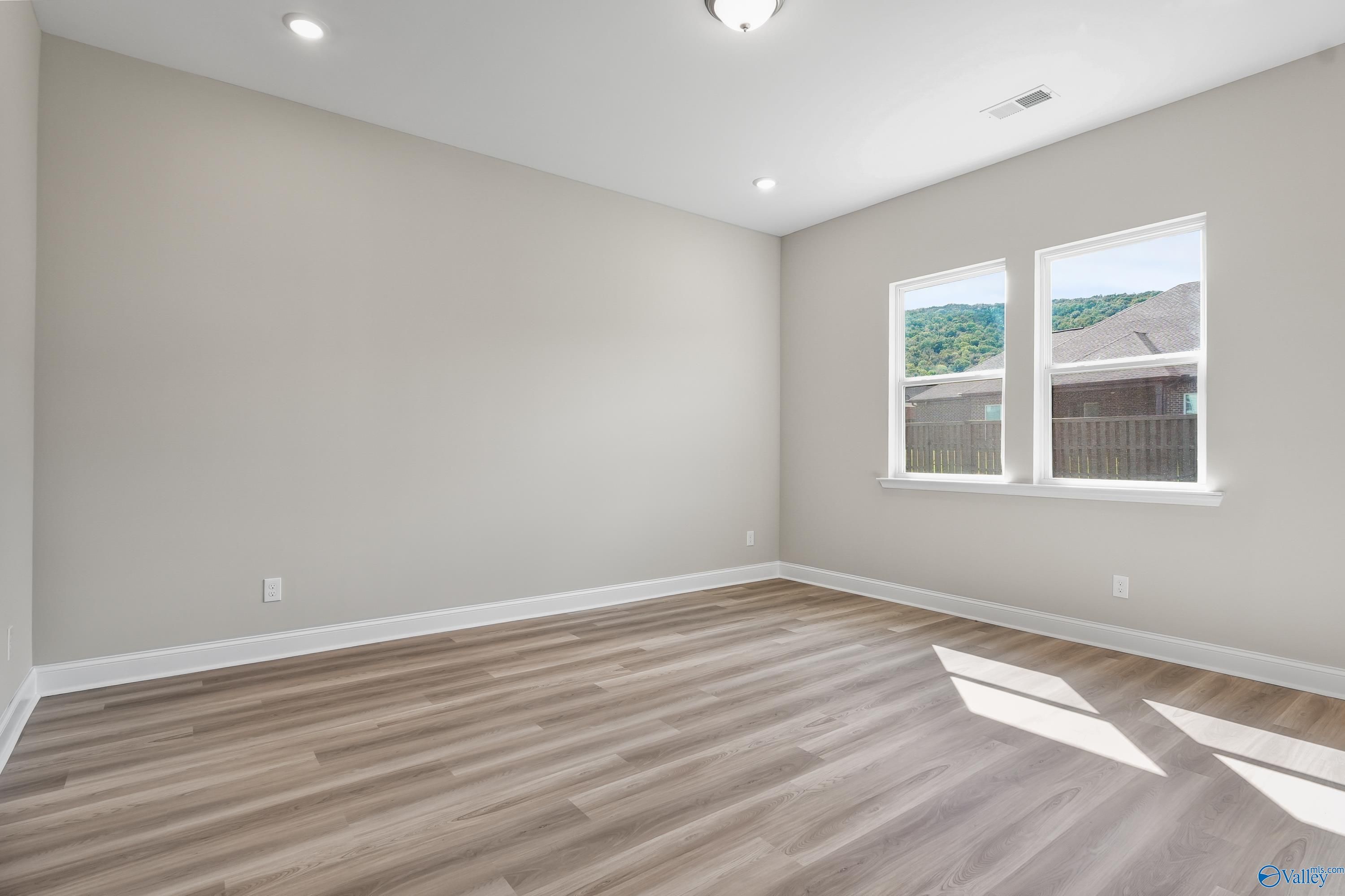 Bright secondary bedroom with light gray walls, LVP hardwood flooring, and hill views in Evermore Homes The Haven, Owens Cross Roads, AL