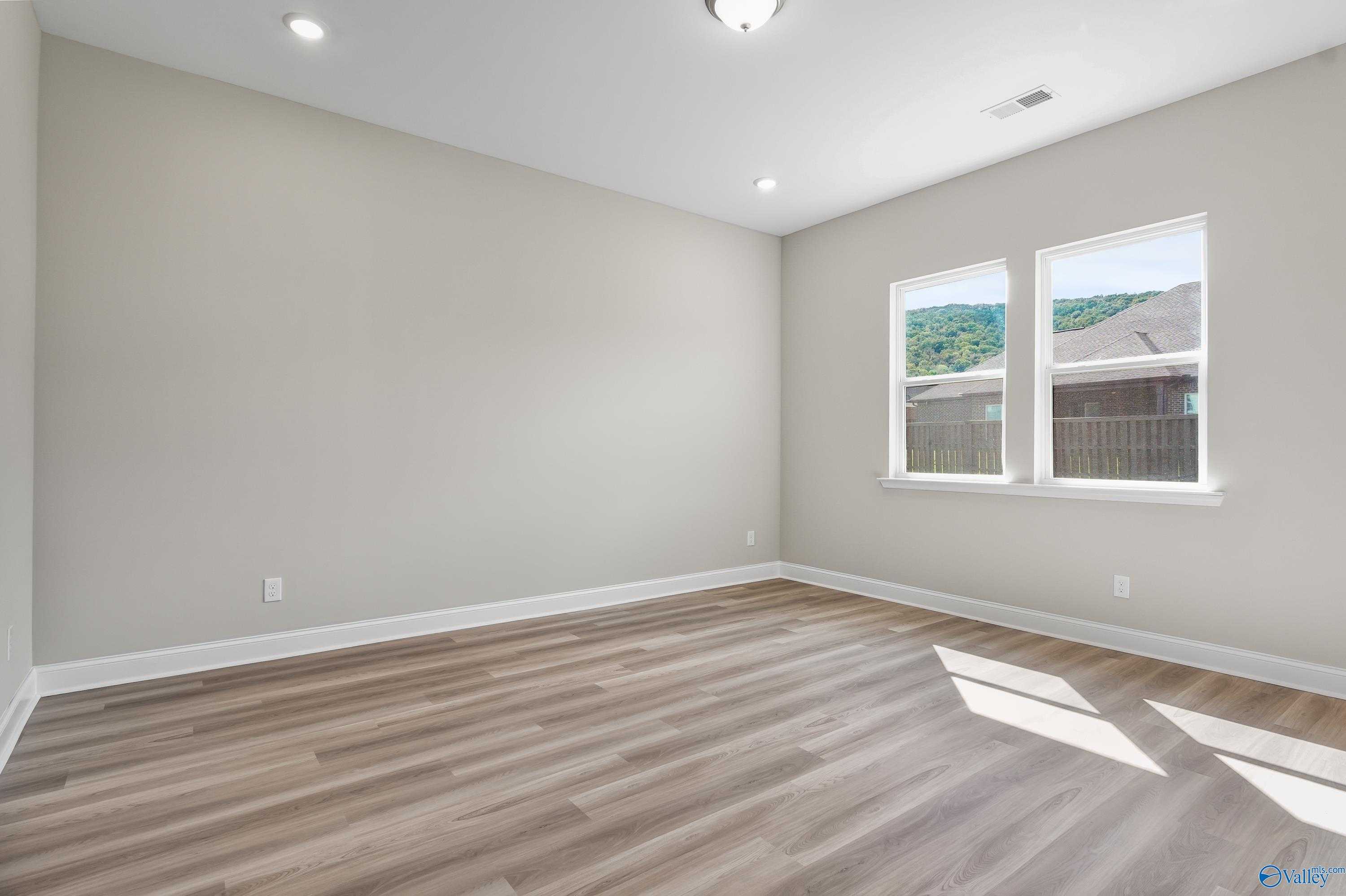 Bright secondary bedroom with light gray walls, LVP hardwood flooring, and hill views in Evermore Homes The Haven, Owens Cross Roads, AL
