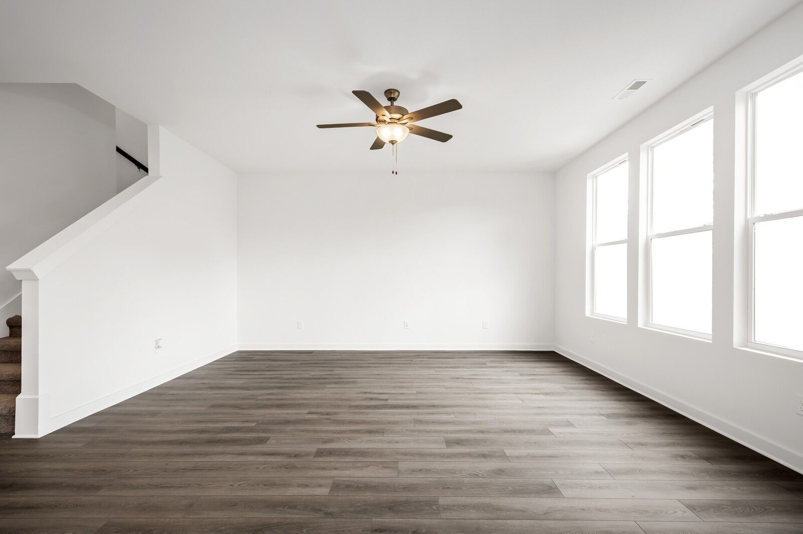 Bright, open living room with wood-look flooring and ceiling fan in The Logan C floor plan at Calista Farms, Tennessee.