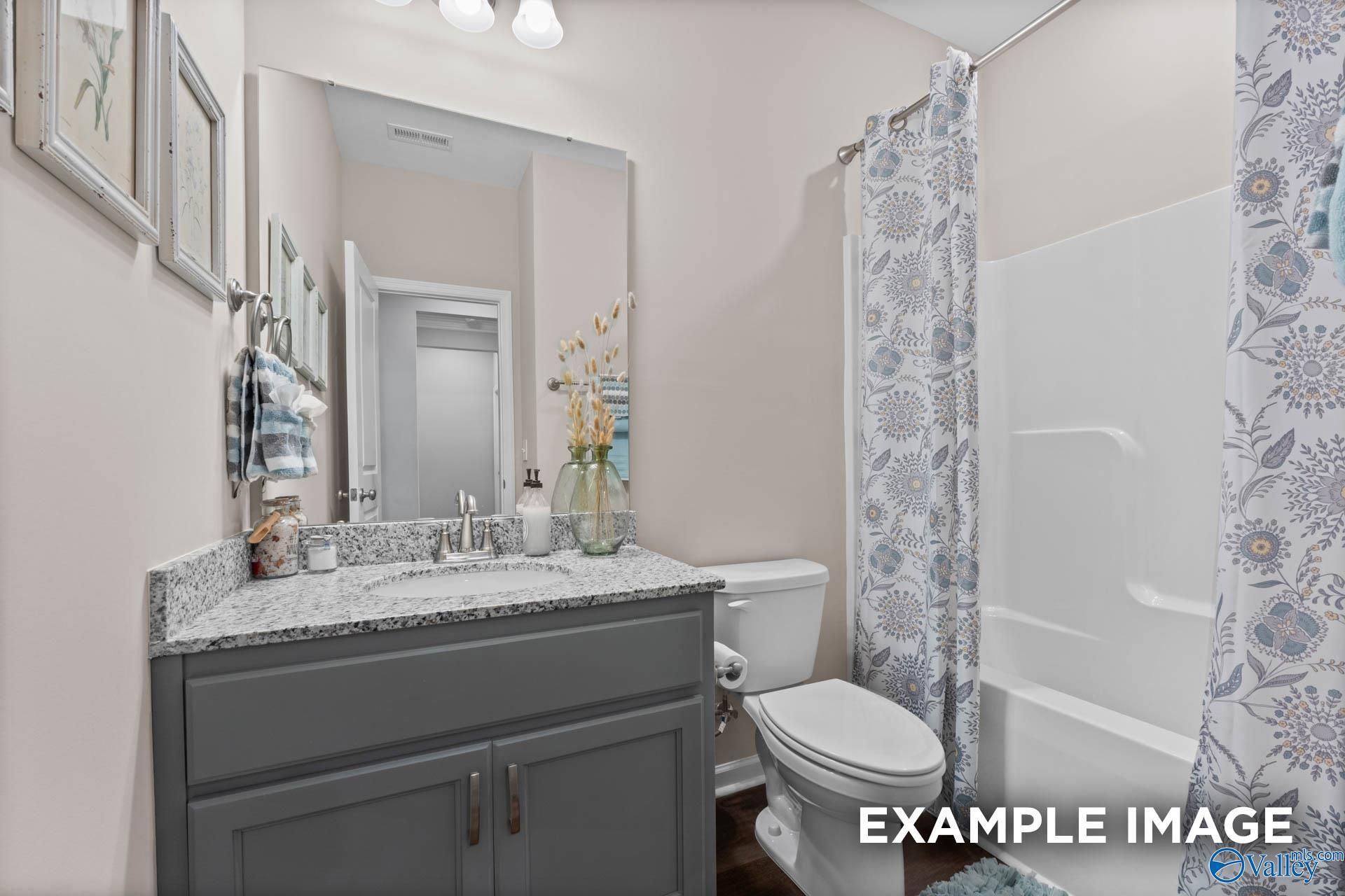 Spacious guest bathroom with gray vanity, large mirror, floral shower curtain in Evermore Homes The Arcadia M, Owens Cross Roads, Alabama