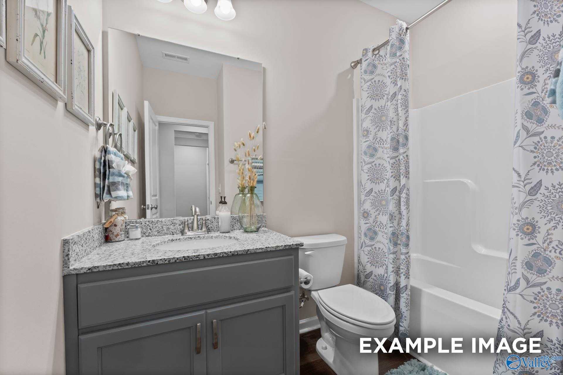 Spacious guest bathroom with gray vanity, large mirror, floral shower curtain in Evermore Homes The Arcadia M, Owens Cross Roads, Alabama