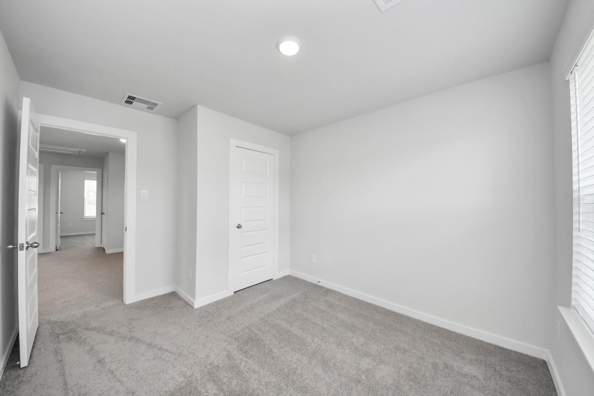 Spacious secondary bedroom with neutral carpet and closet in The Brazos F floor plan at Liberty Estates, Cleveland, Texas.
