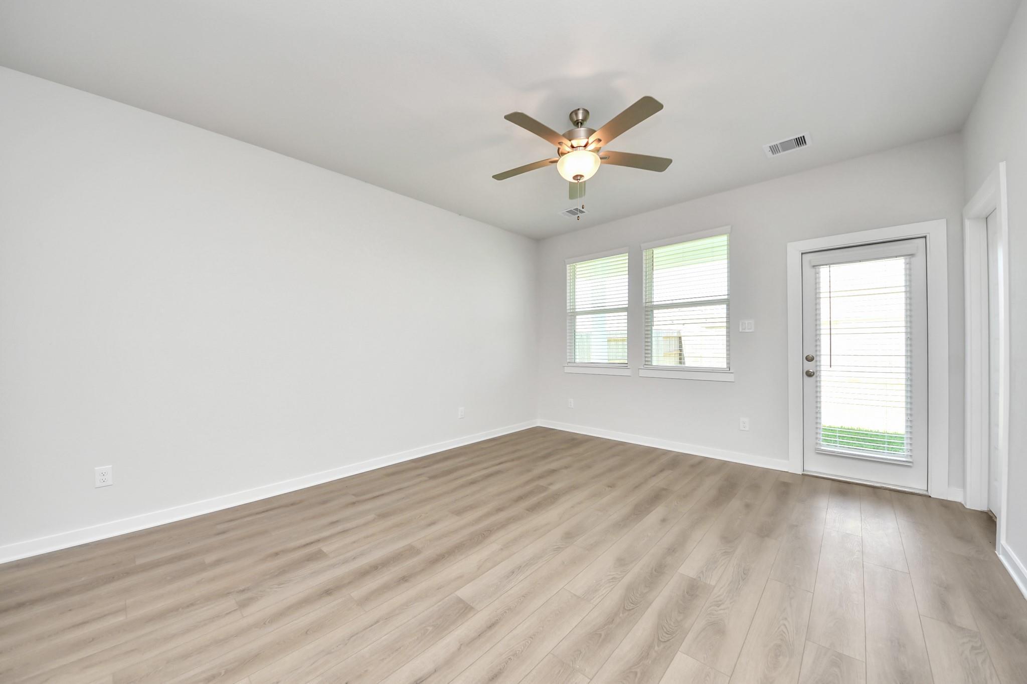 Bright empty room with luxury vinyl plank flooring, ceiling fan, windows, and glass back door in Davidson Homes Costa A, Beasley TX