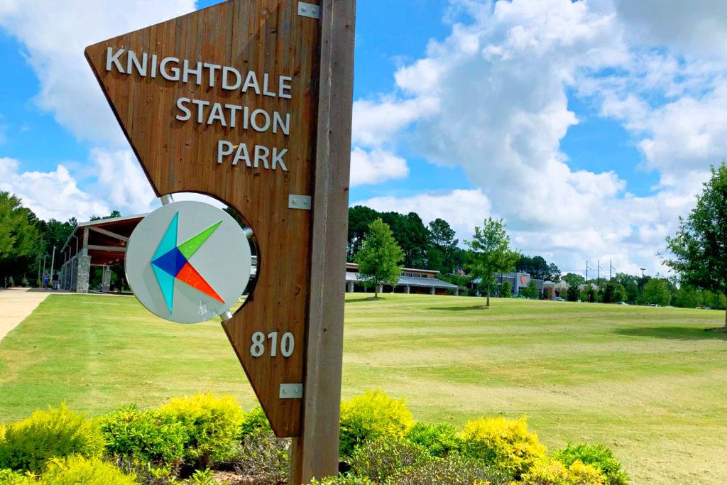 Knightdale Station Park sign in Knightdale NC with wooden post, logo, address 810, green lawns, trees, and modern pavilion