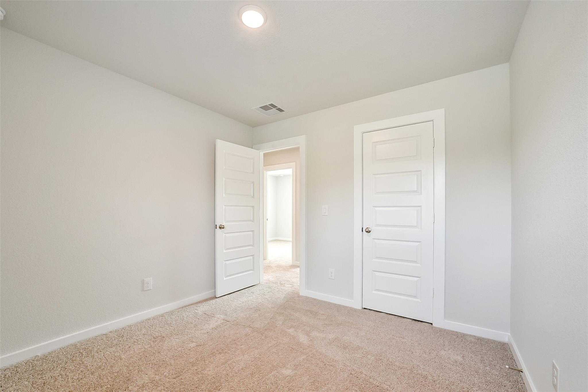 Bright secondary bedroom with light gray walls, beige carpet, and open white door to hallway in Davidson Homes The Blanco E, Magnolia, Texas