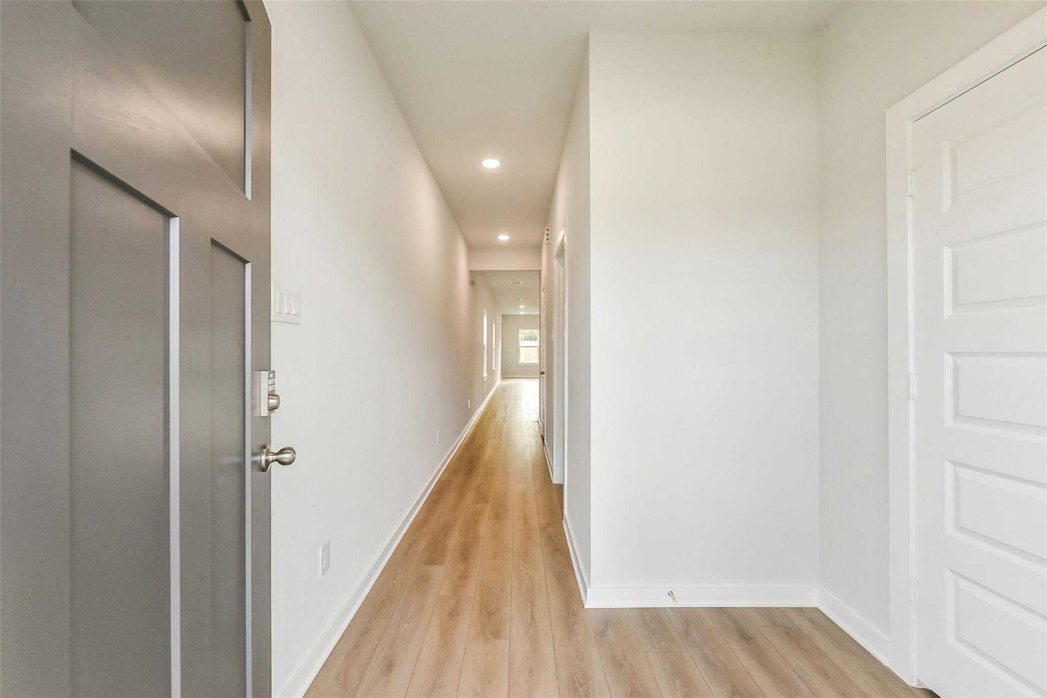 Bright entry hallway with gray front door, light oak floors, and white walls in The Frio G home, Dayton Texas