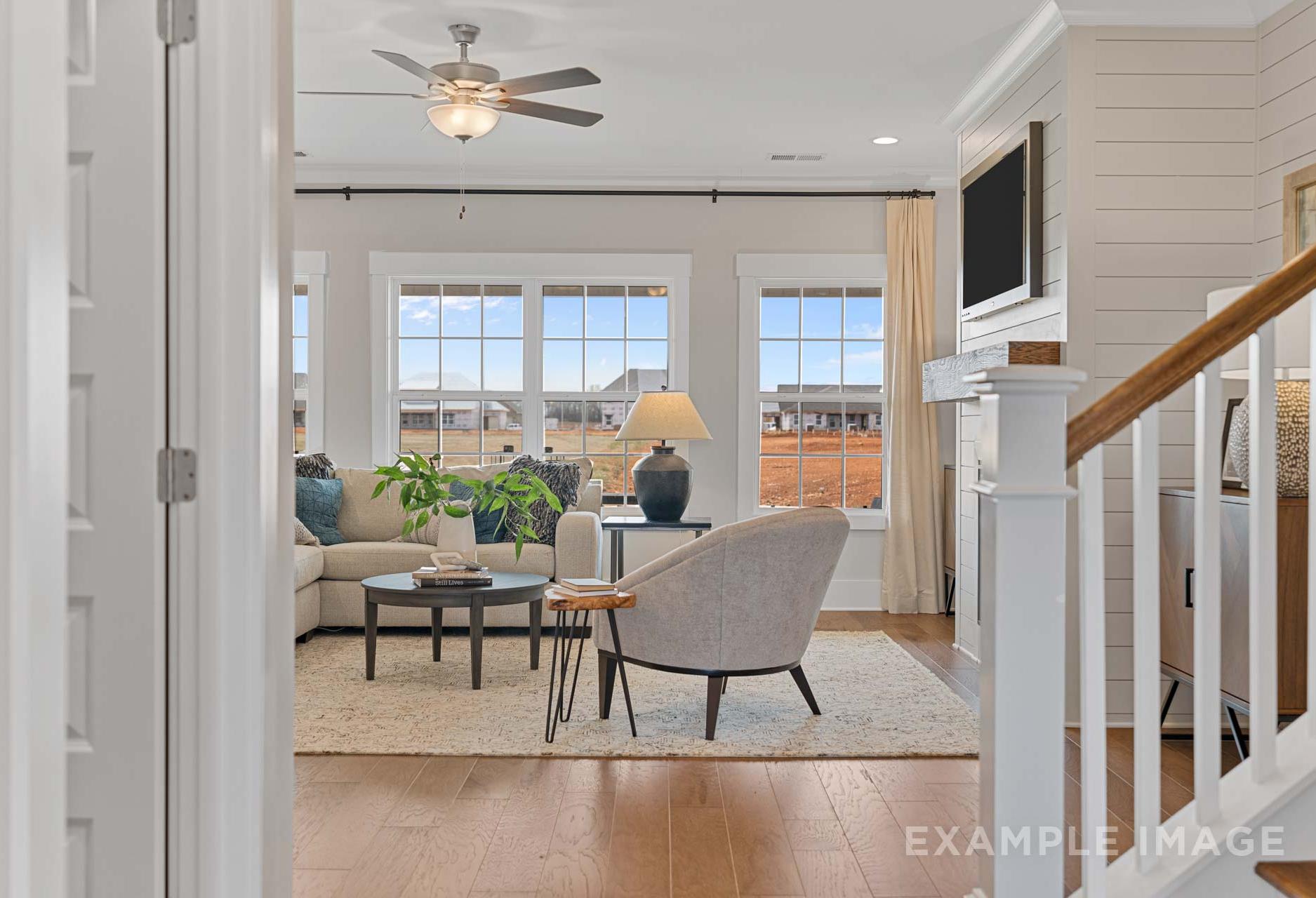 Spacious open-concept living room in The Rockford home with large windows, sectional sofa, fireplace, and white staircase
