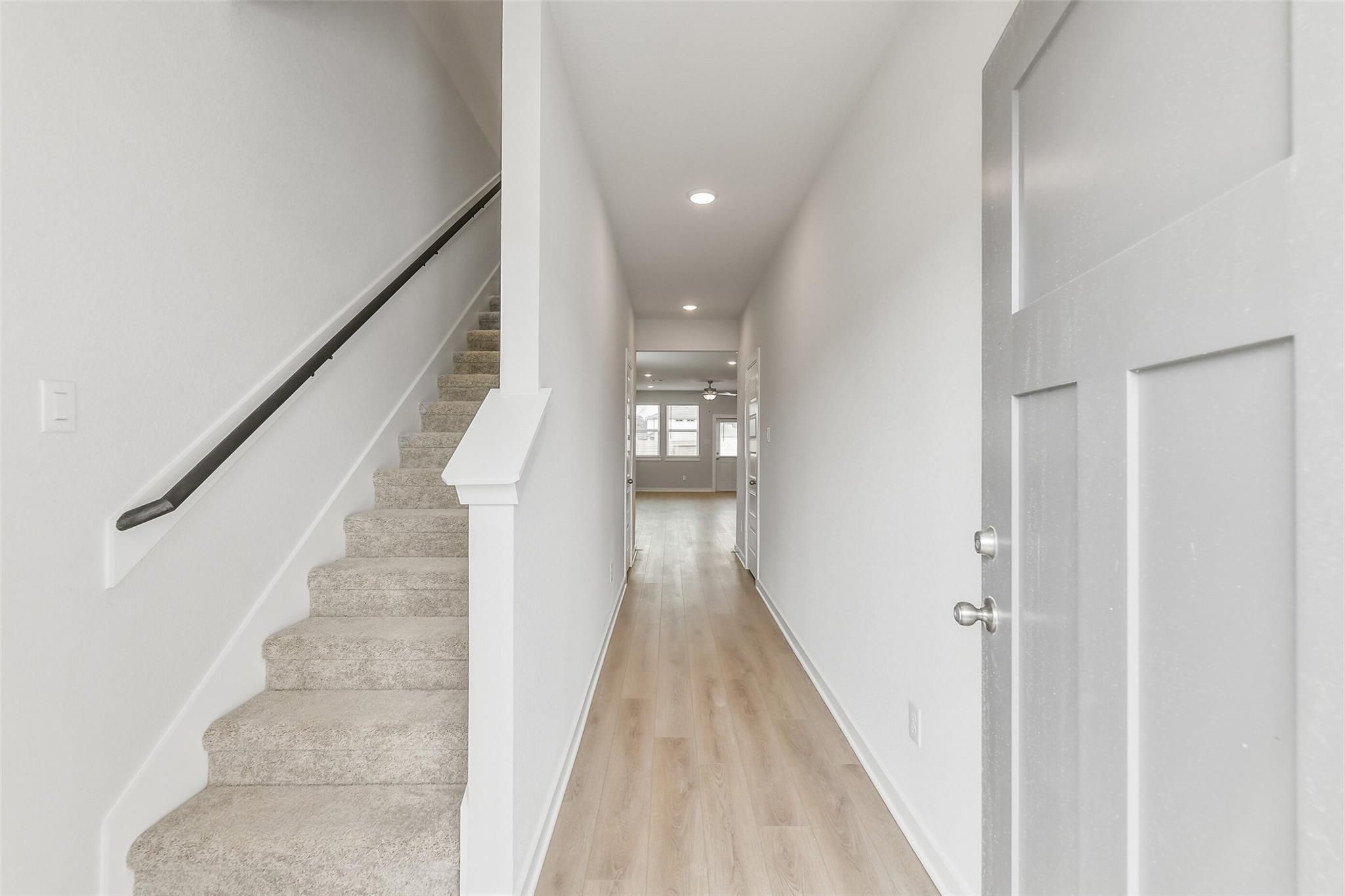 Bright hallway with carpeted staircase, light oak floors, and open doorways in 5-bedroom The Brazos E home, Cleveland, Texas