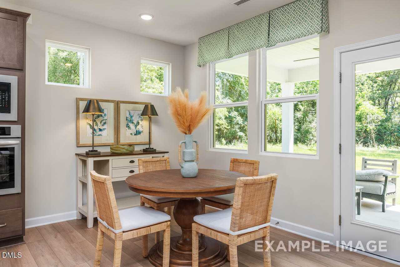 Bright dining nook with round wooden table, wicker chairs, pampas grass vase, and lush backyard views in Lillington, NC home